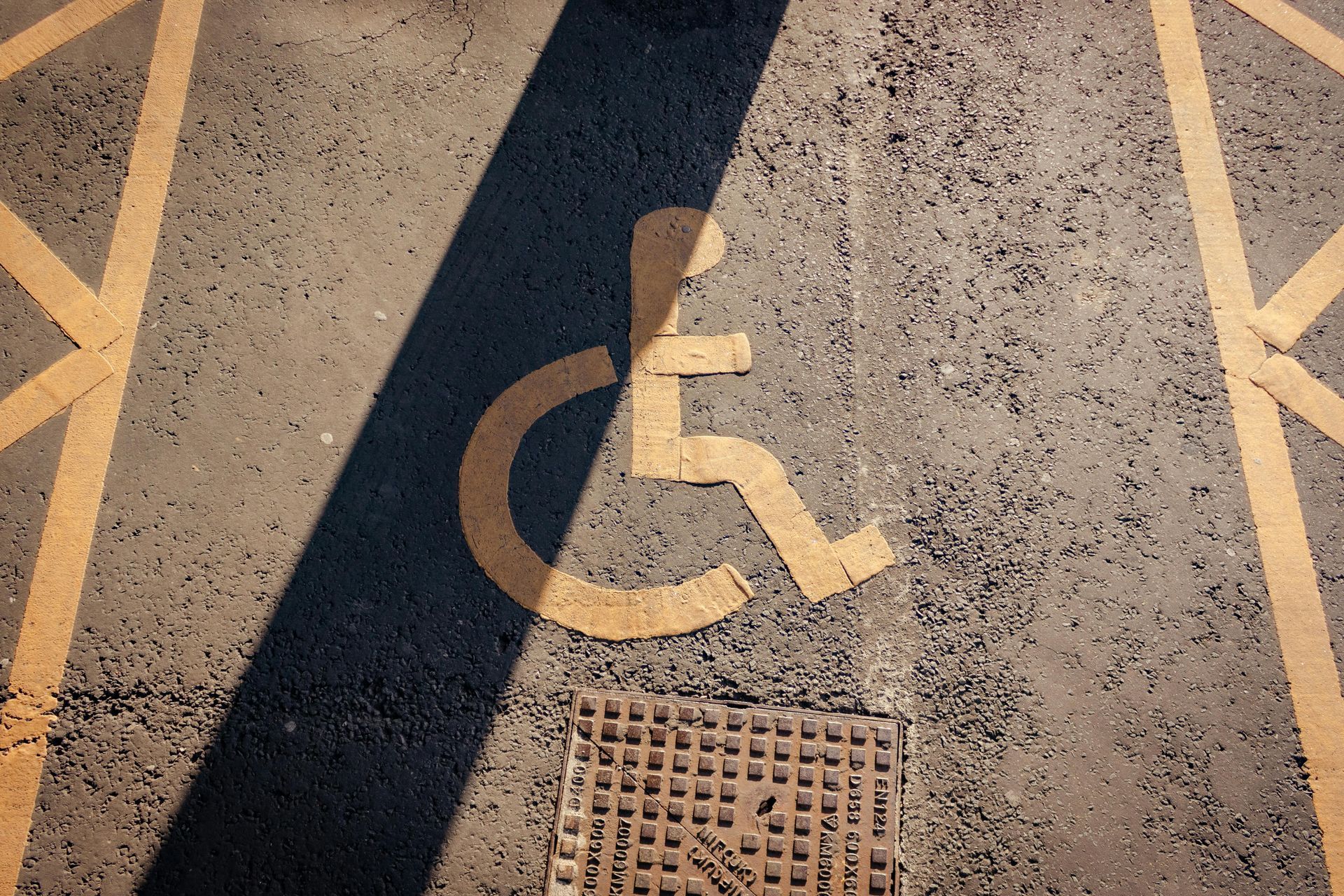 Accessible parking space with a painted wheelchair symbol on asphalt and a drain cover nearby