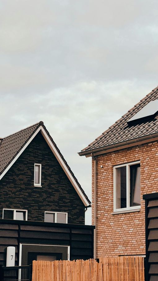 Two houses with dark roofs and brick siding beneath a cloudy sky