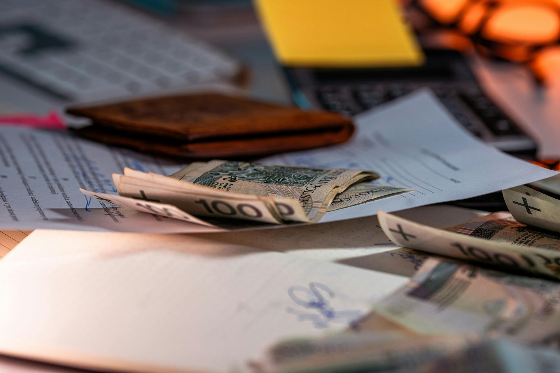 Stacked U.S. dollar bills on paperwork beside a wallet and calculator on a desk