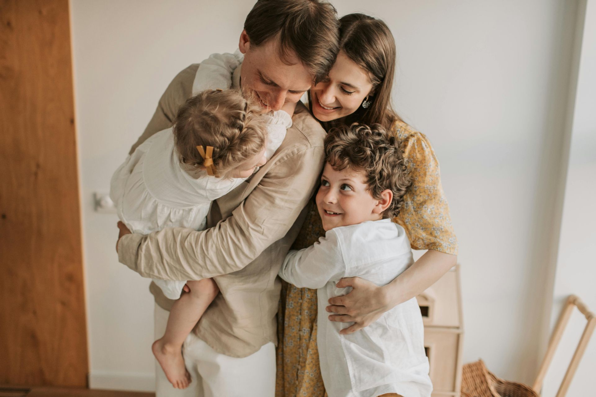 Family hugging in a bright room, with two adults embracing two smiling children.