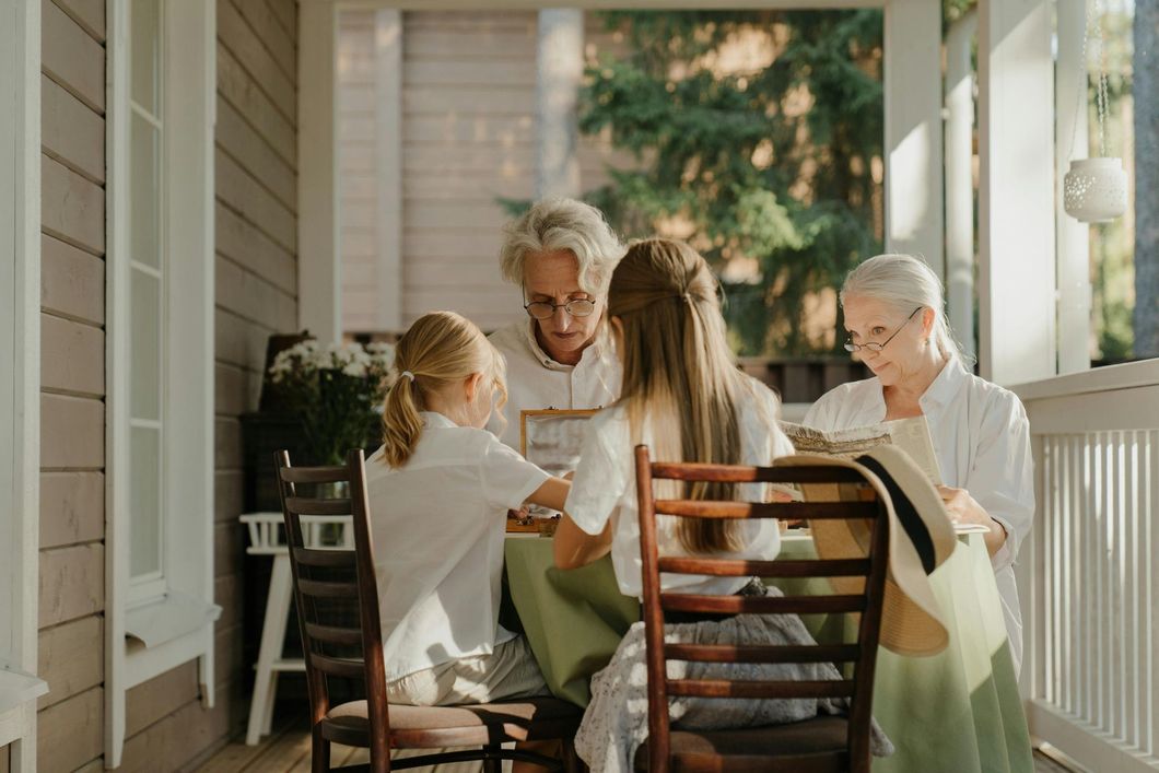 Three people sitting on a porch, looking at an open book together in soft daylight