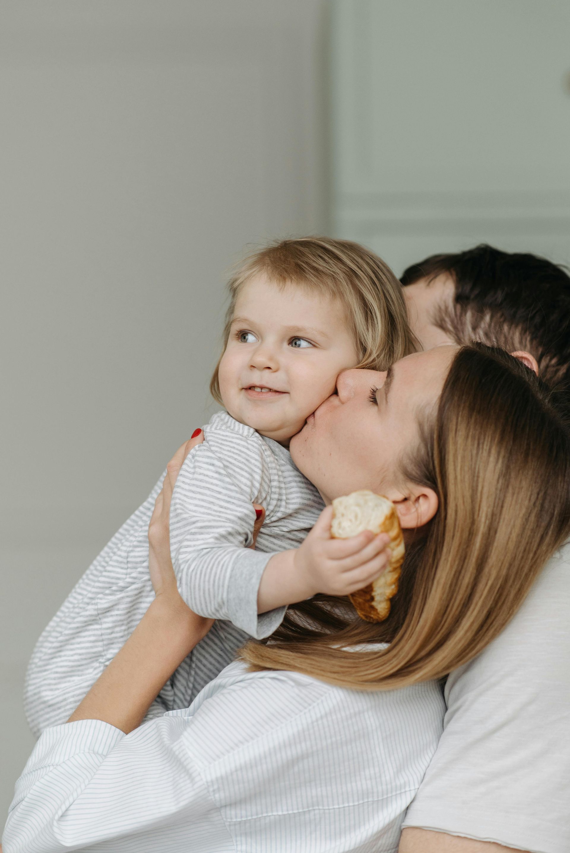 Woman hugging and kissing a smiling child in a light-filled room