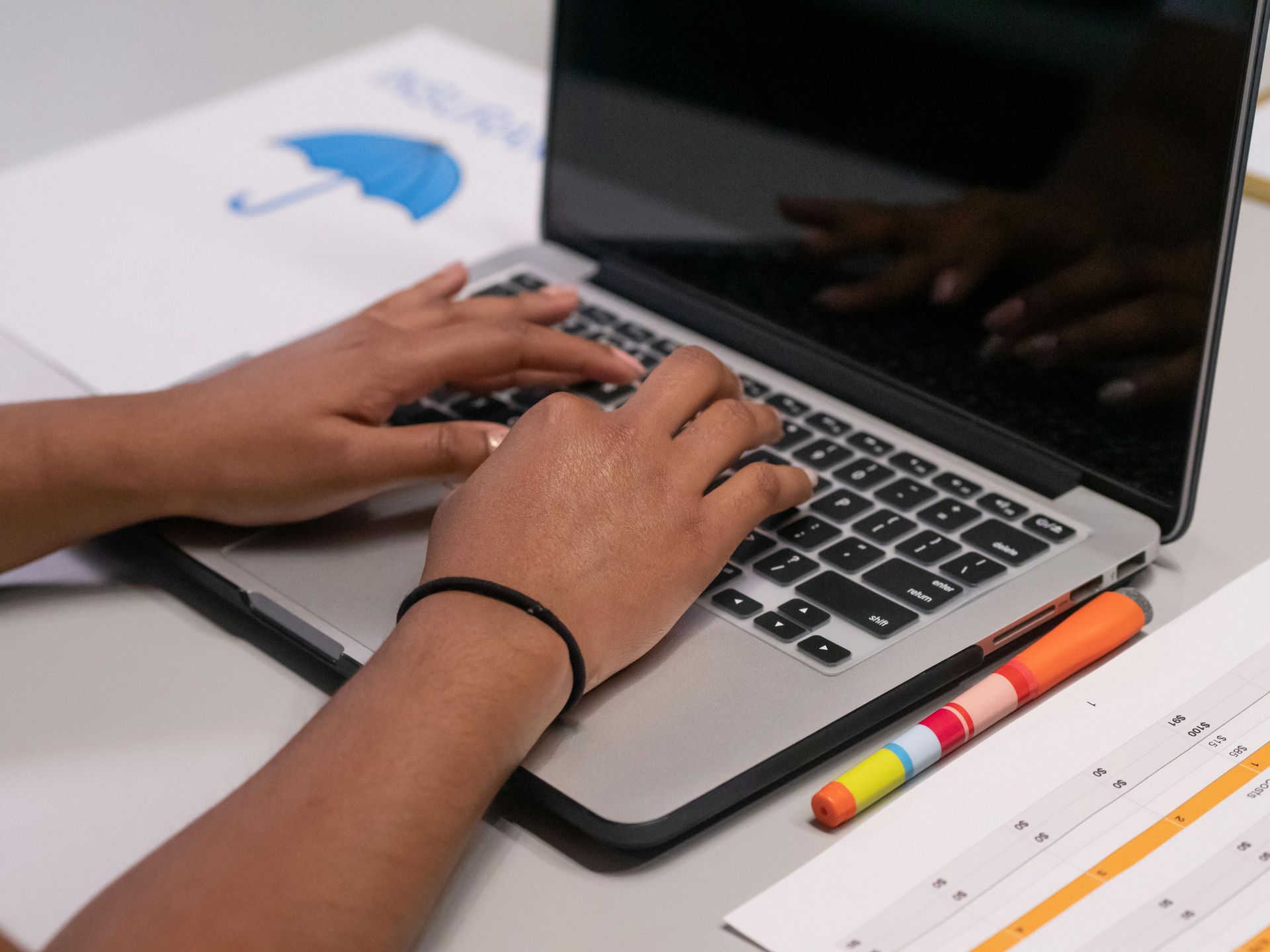 Hands typing on a laptop beside colored pencils and a notebook on a desk