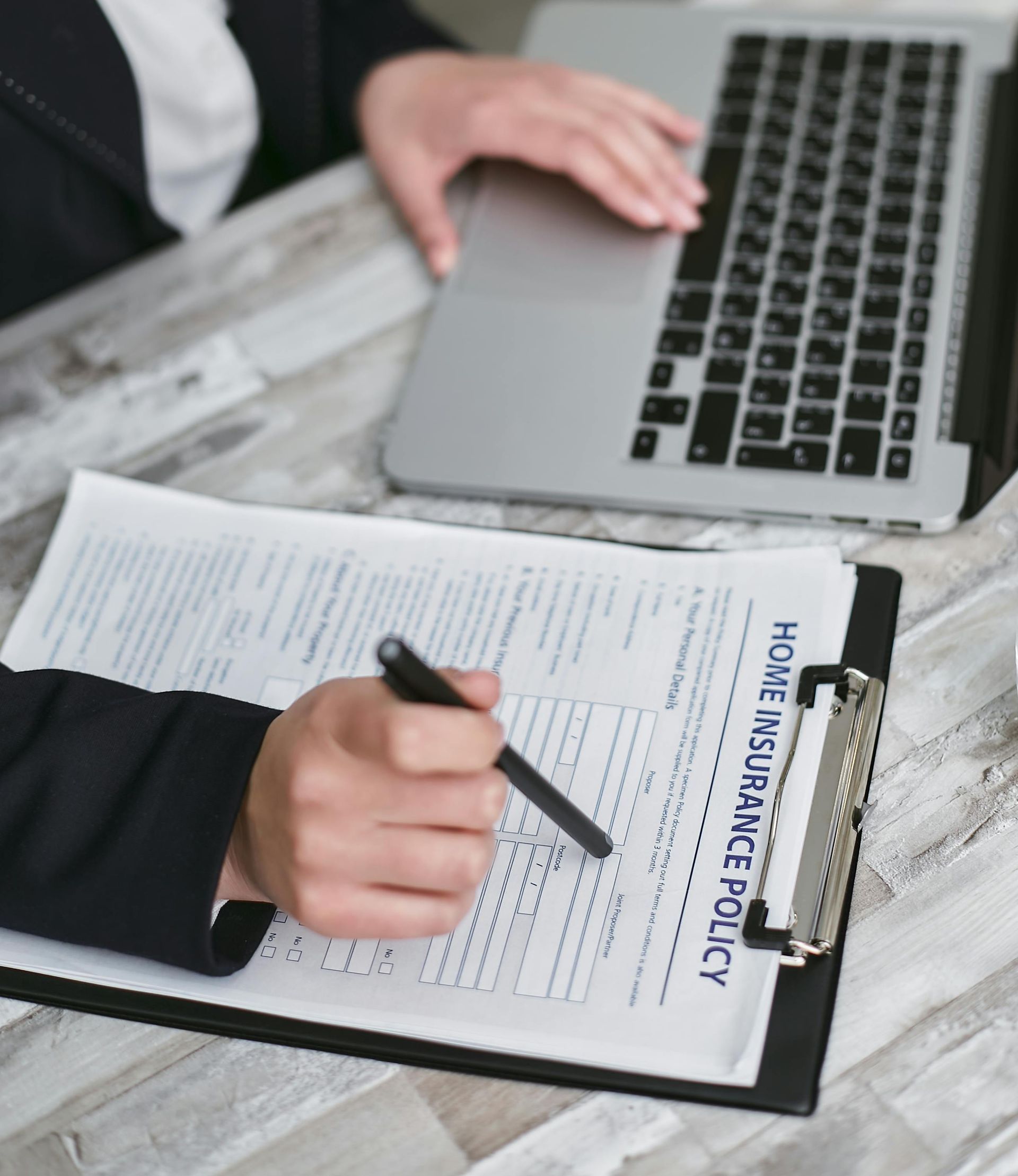 Person reviewing policy document on a clipboard beside a laptop, with pen in hand