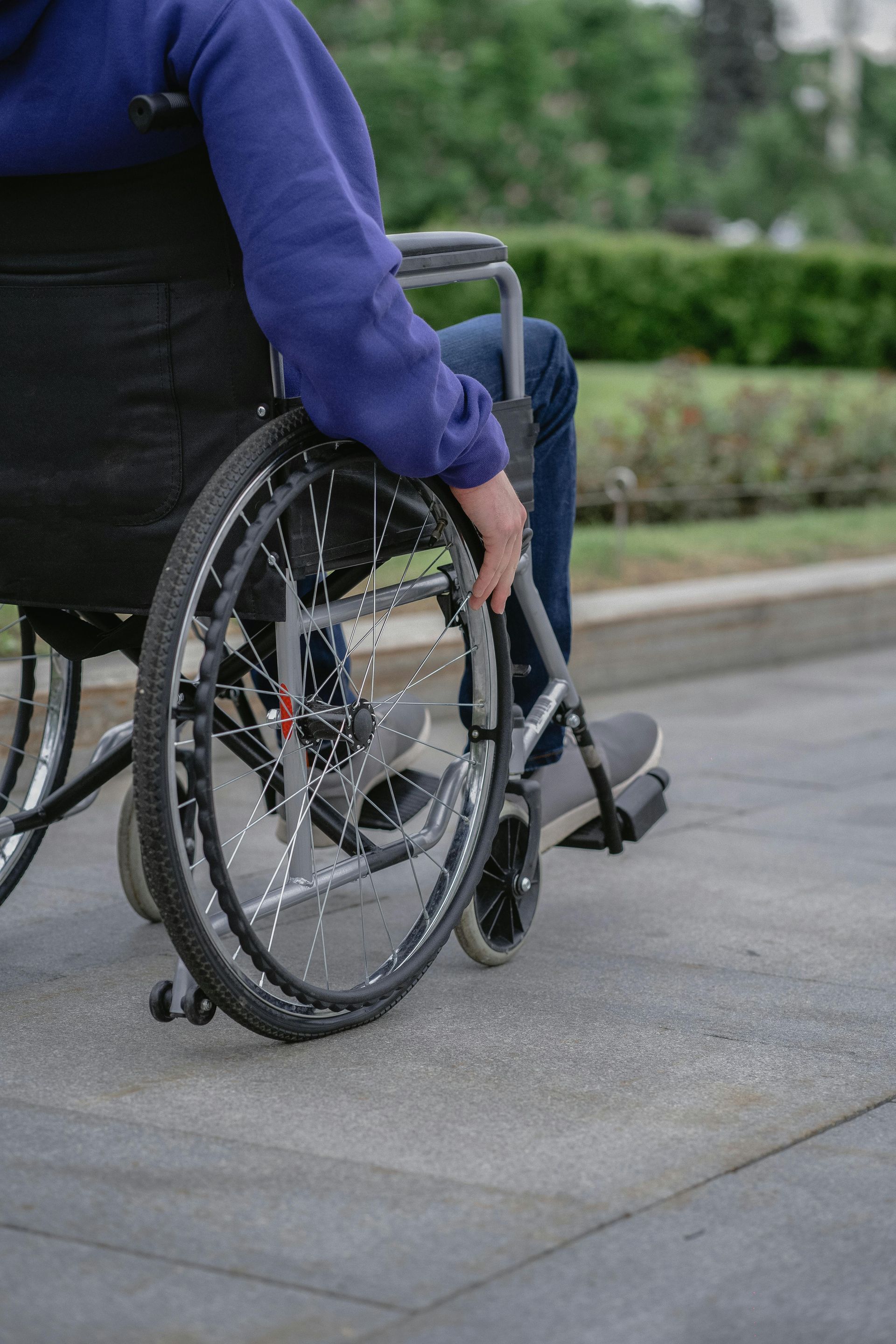 Person pushing a wheelchair along a sidewalk next to a hedge
