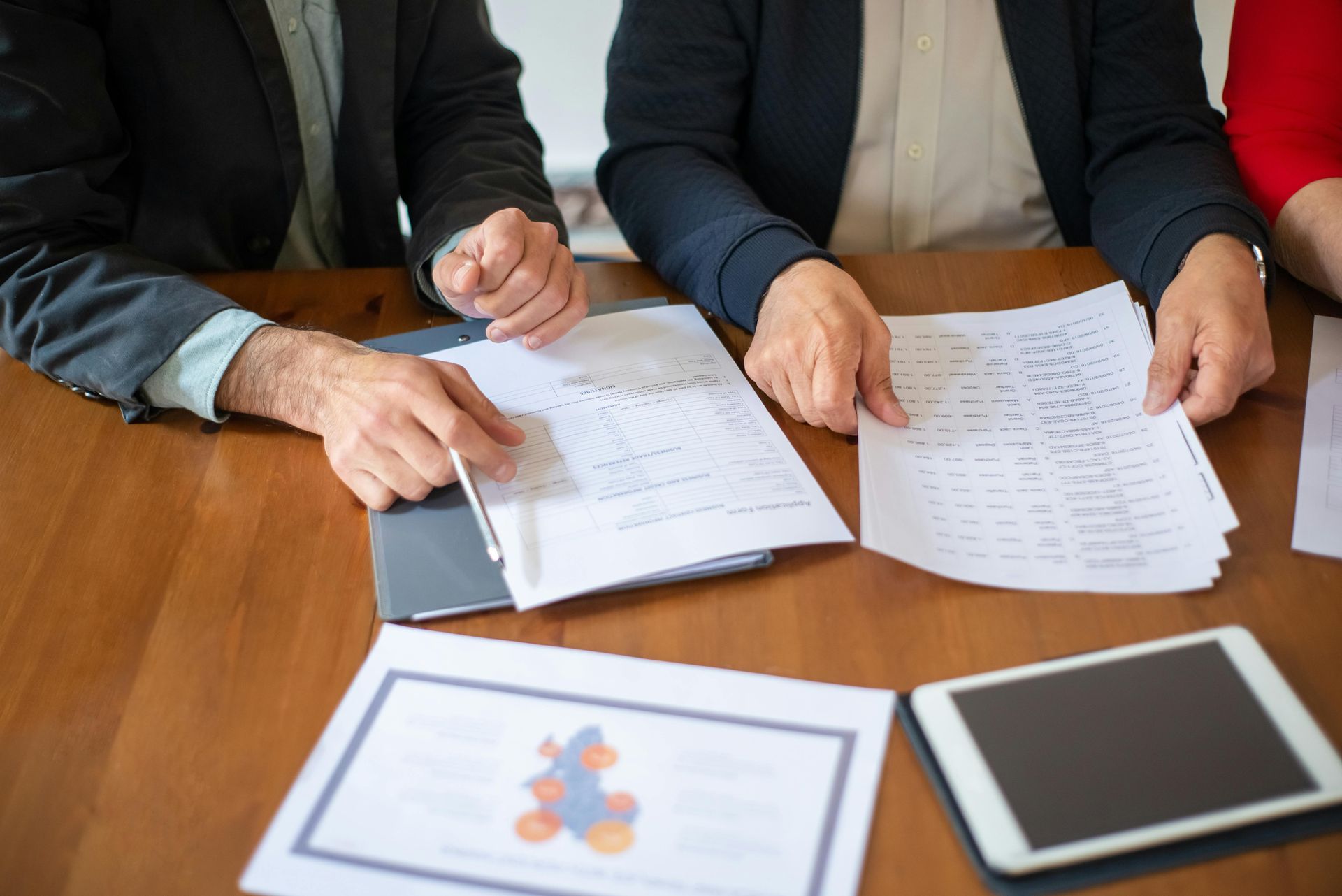 Three people reviewing printed charts and documents at a wooden table with a tablet nearby