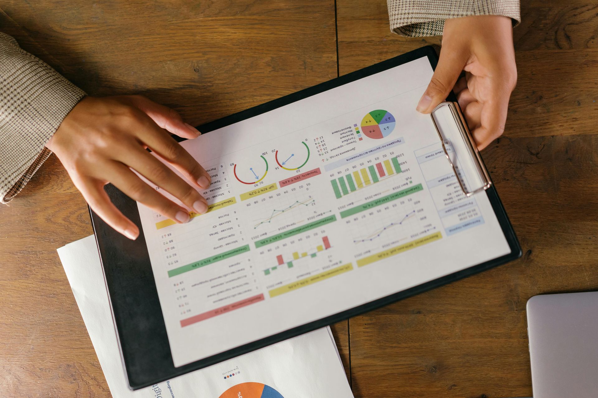 Hands reviewing a clipboard with colorful charts and graphs on a wooden desk
