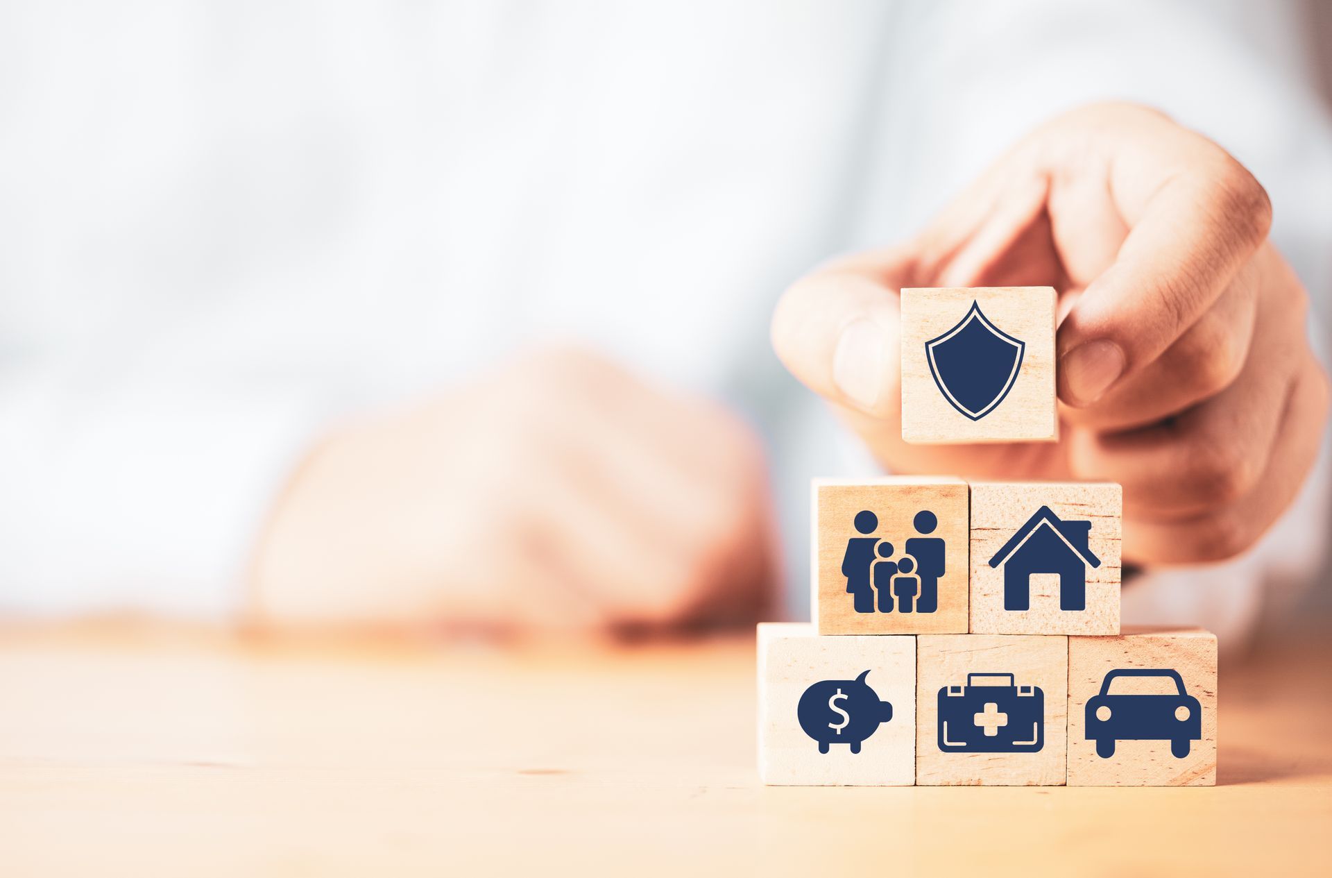 Stack of wooden blocks with insurance icons in a hand, including home, family, car, health, and money symbols.