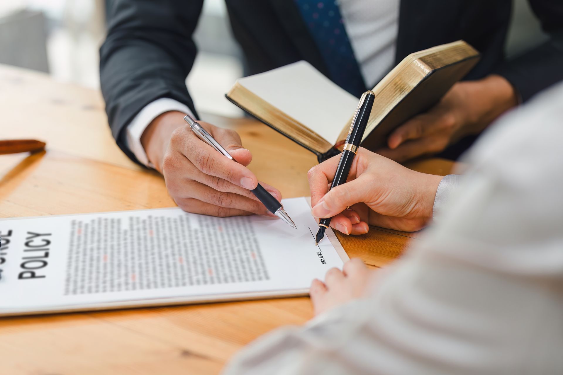 Hands signing a policy document at a desk with a notebook in the background