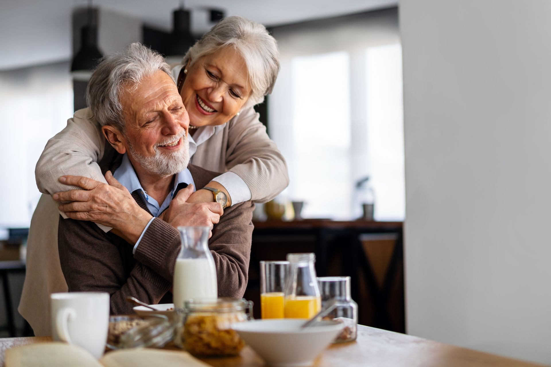 Smiling older couple hugging at a breakfast table with orange juice and coffee