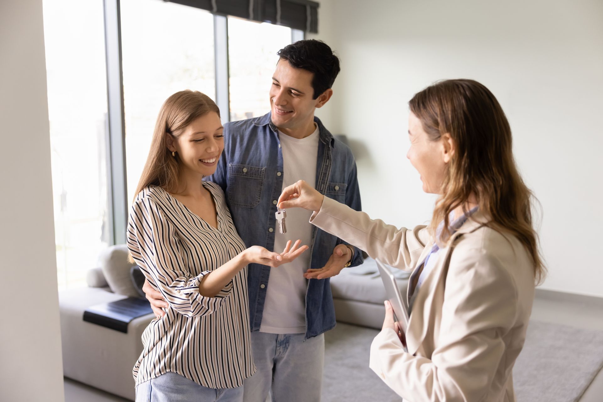 Three people talking in a bright living room, with one woman handing over keys.