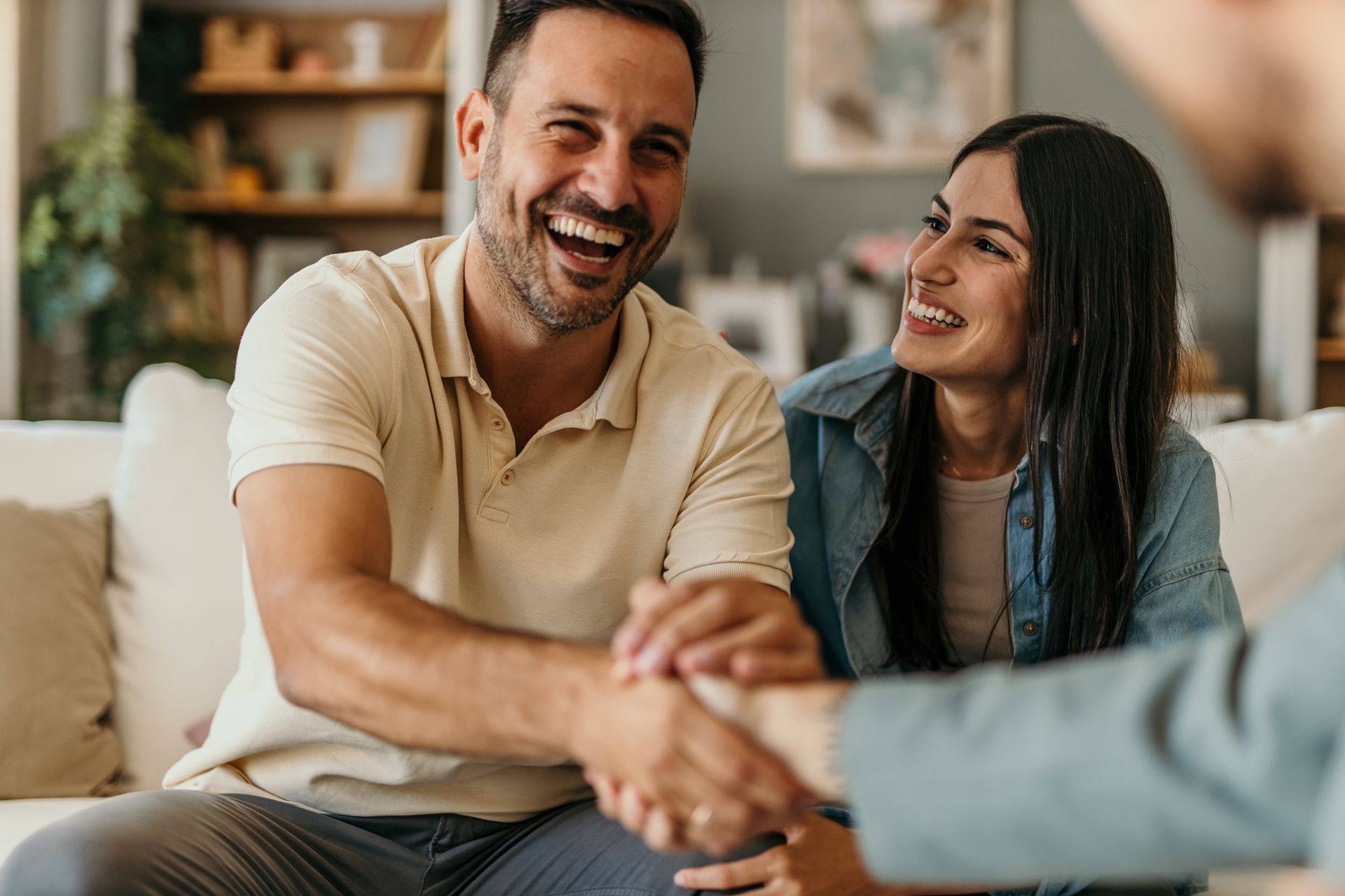 Two people smiling and shaking hands in a cozy indoor setting