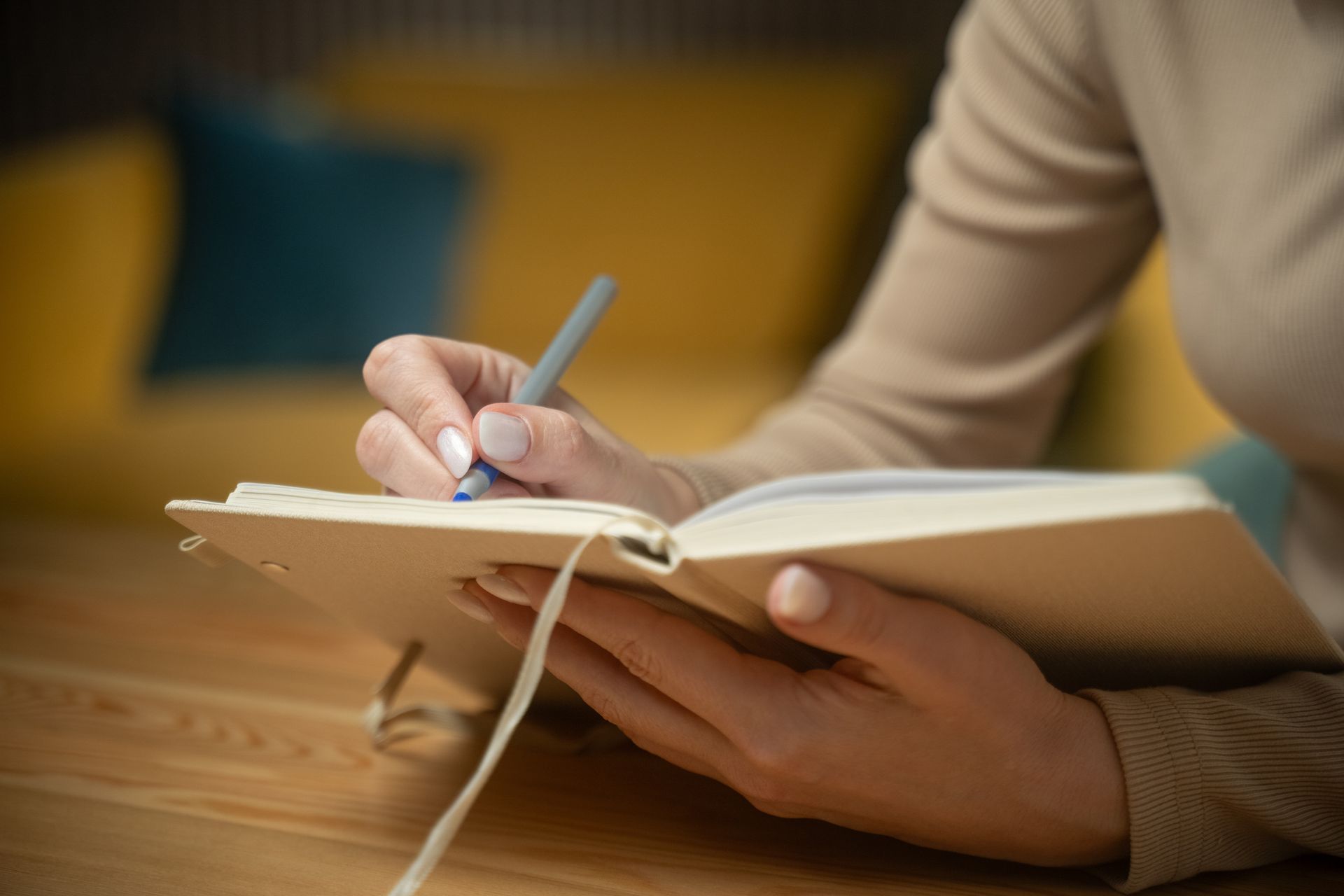 Hands writing in a notebook on a wooden table with a pen, in a cozy indoor setting.