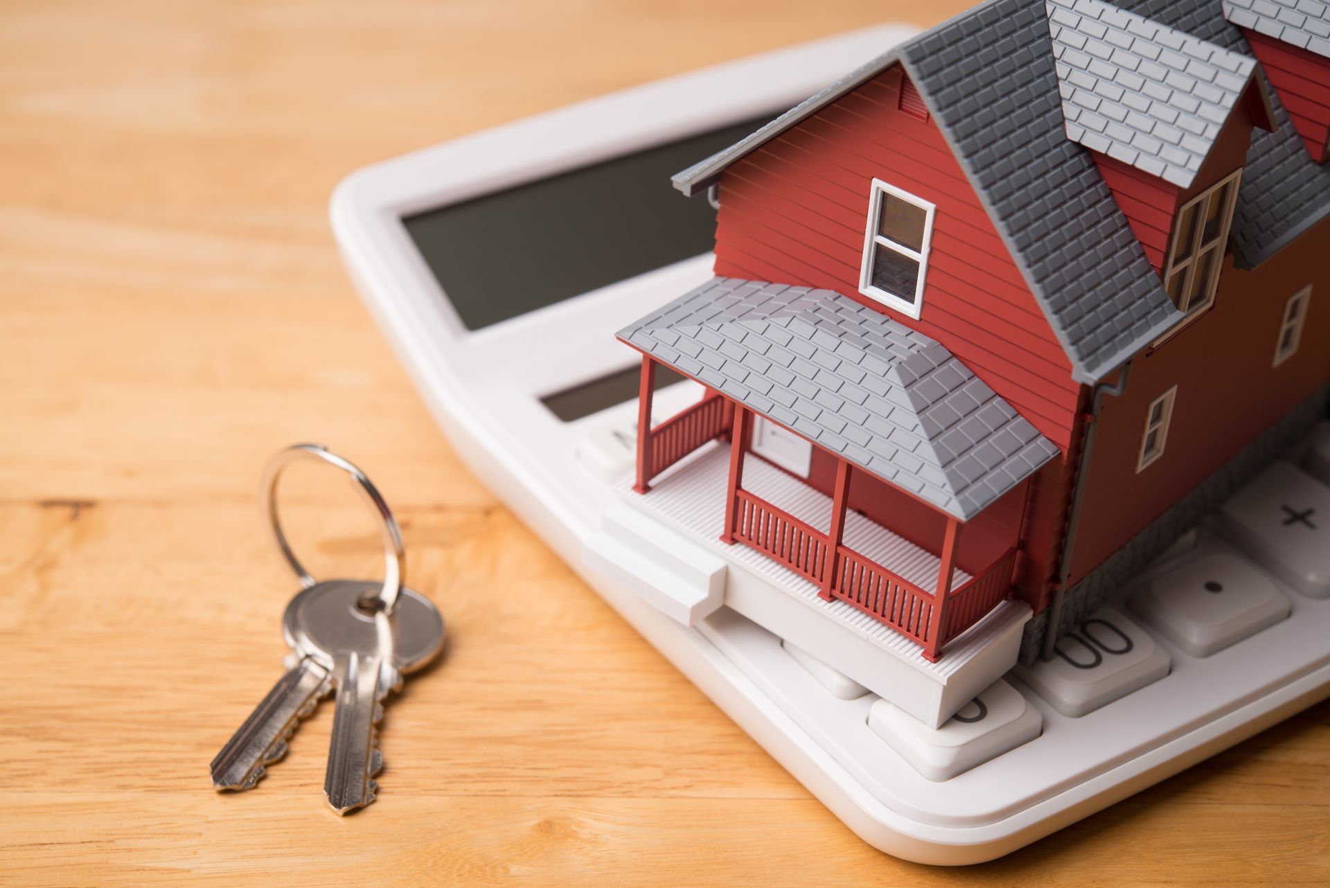 Miniature red house model on a white calculator, with a keyring beside it on a wooden surface