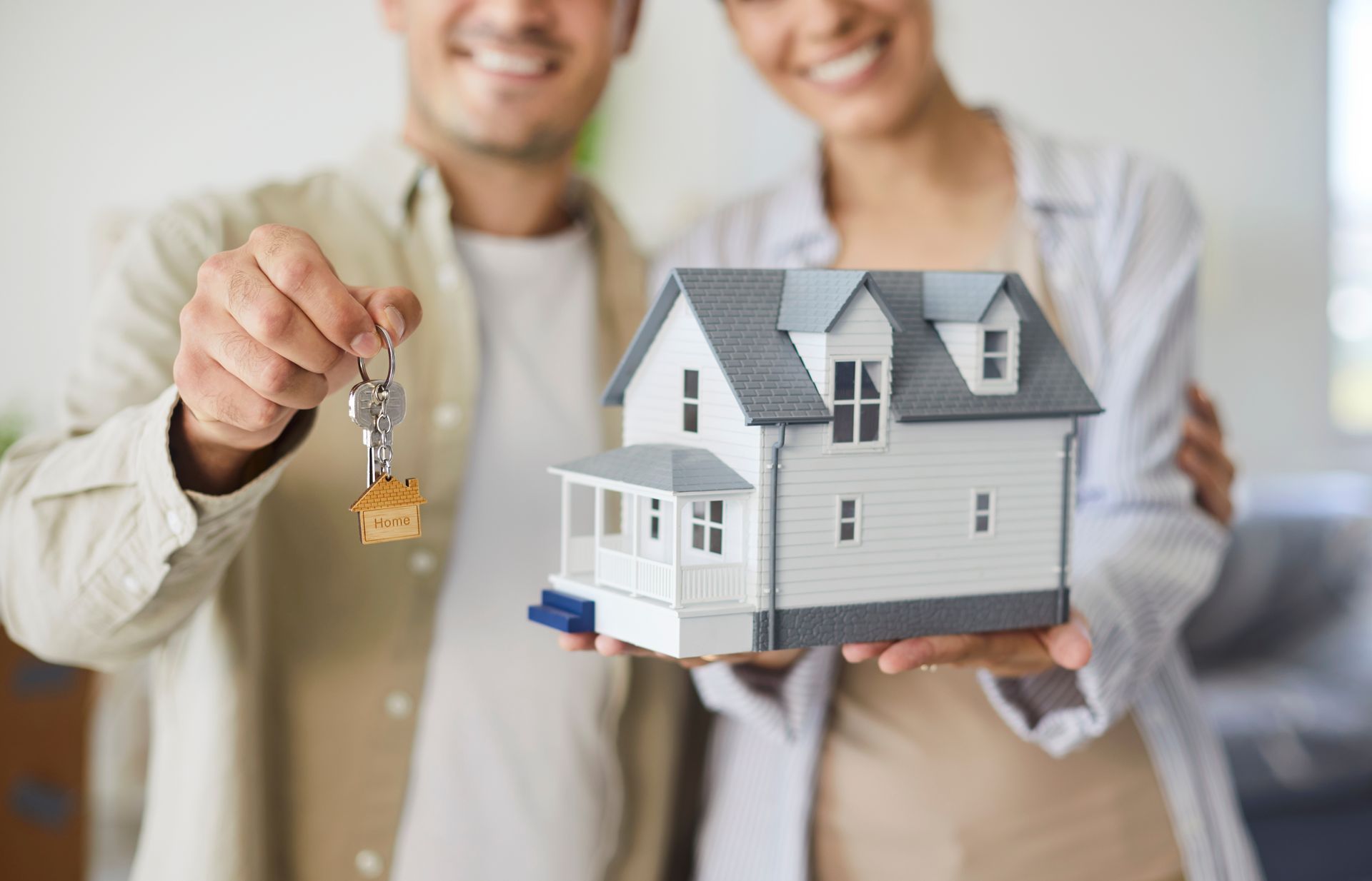 Hands holding a house key and a small model house, suggesting a home purchase or real estate sale.