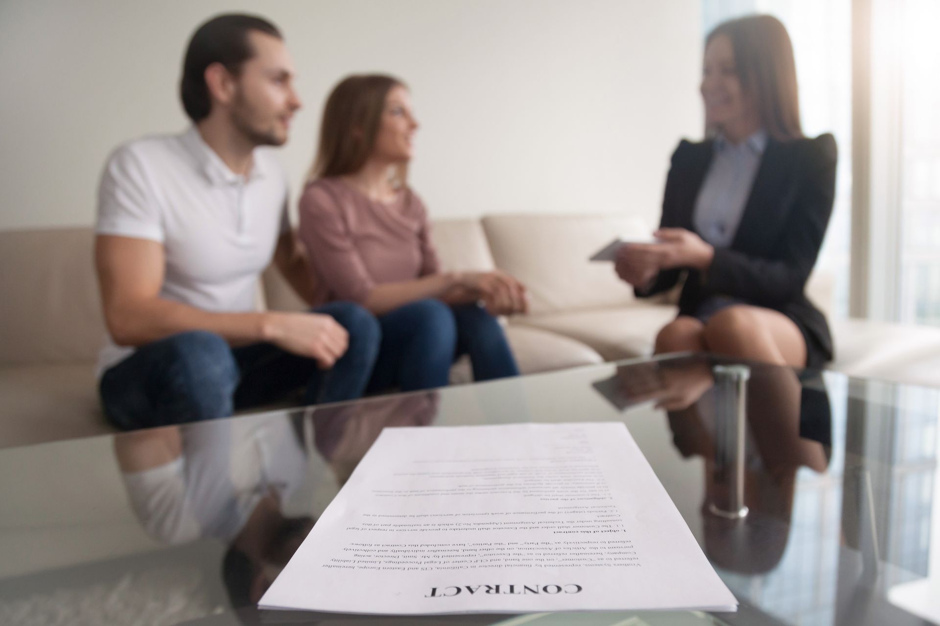 Two people talking with a therapist across a glass table, with a document in the foreground.