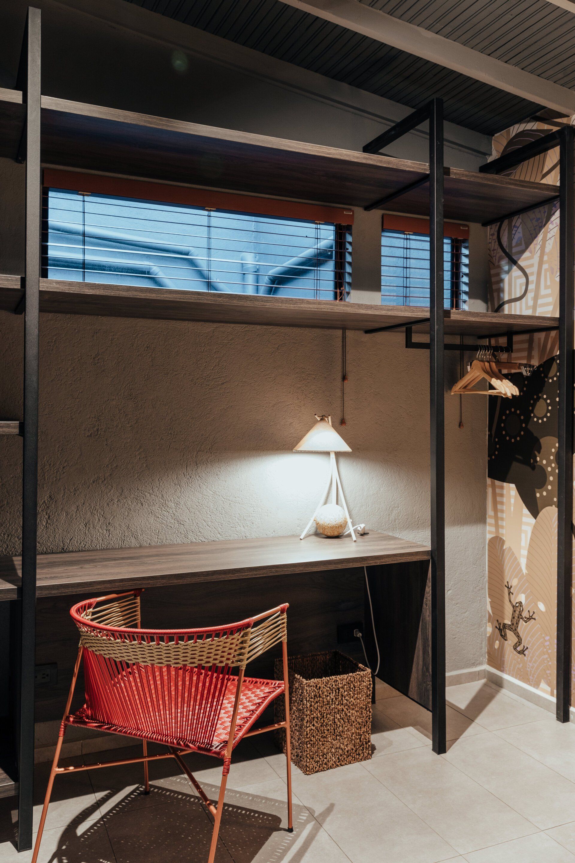 Una habitación con un escritorio, una silla, una lámpara y estantes.