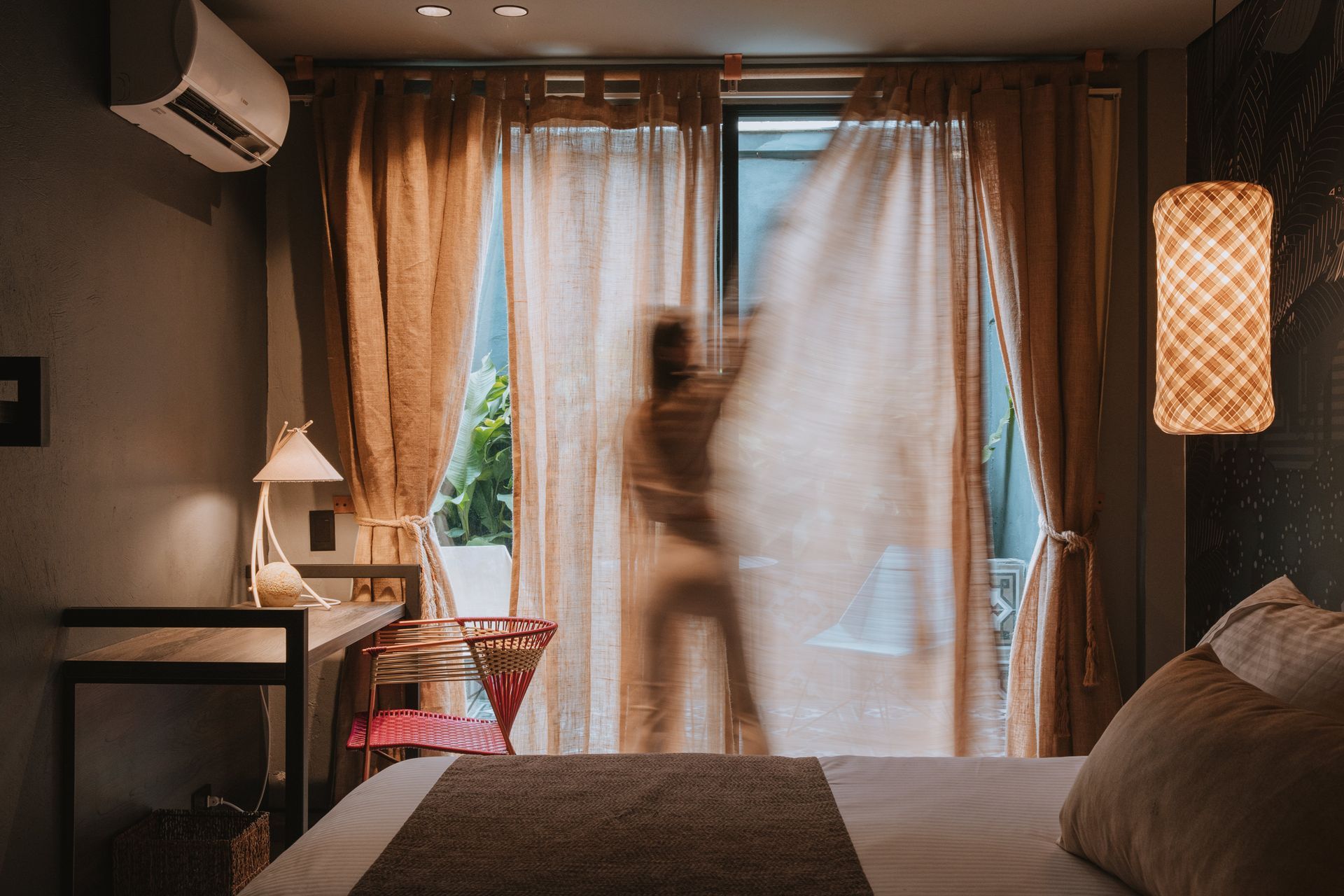 Una imagen borrosa de una persona parada frente a una ventana en un dormitorio.