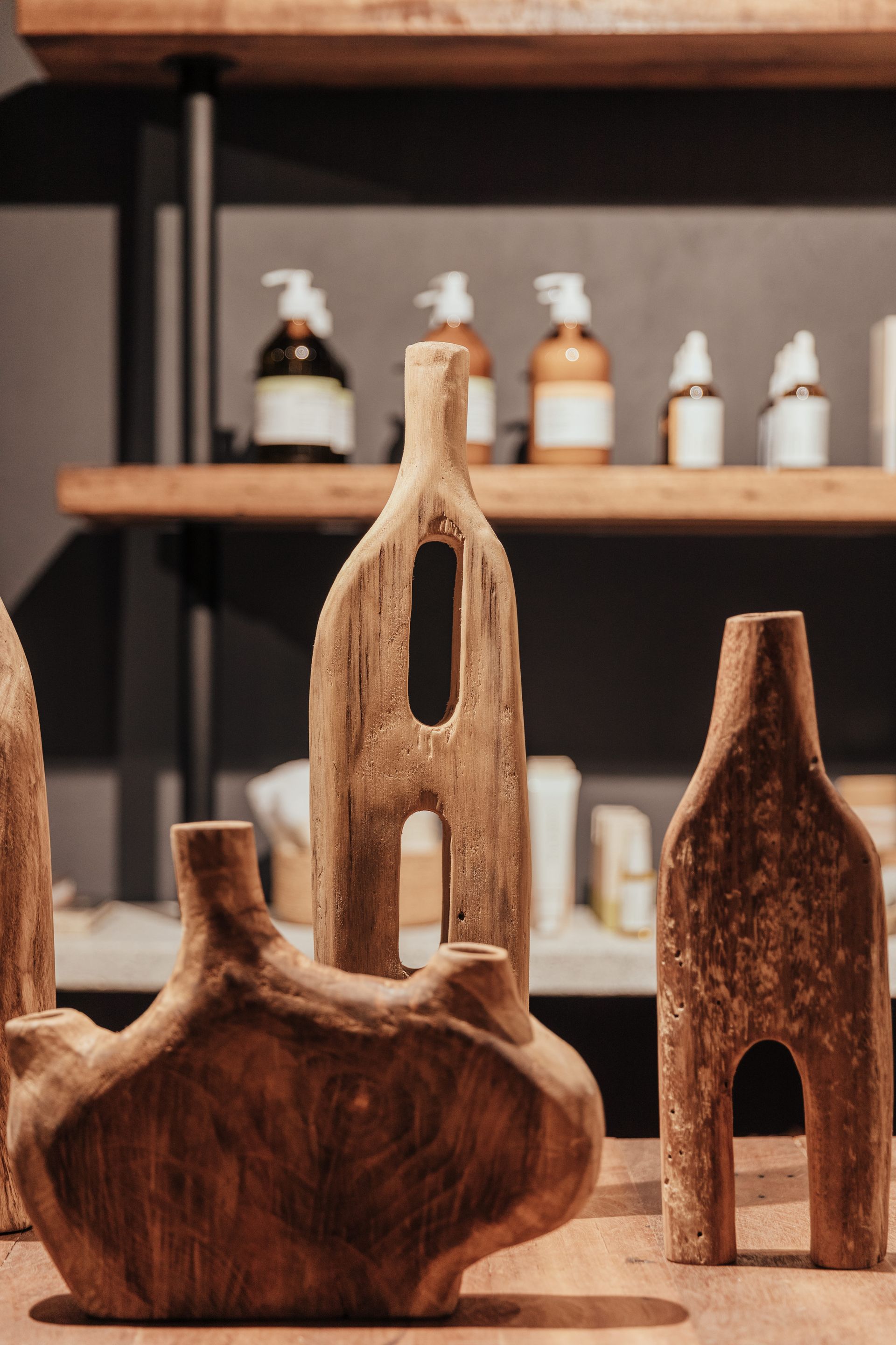 Un grupo de jarrones de madera están colocados sobre una mesa frente a un estante con botellas encima.