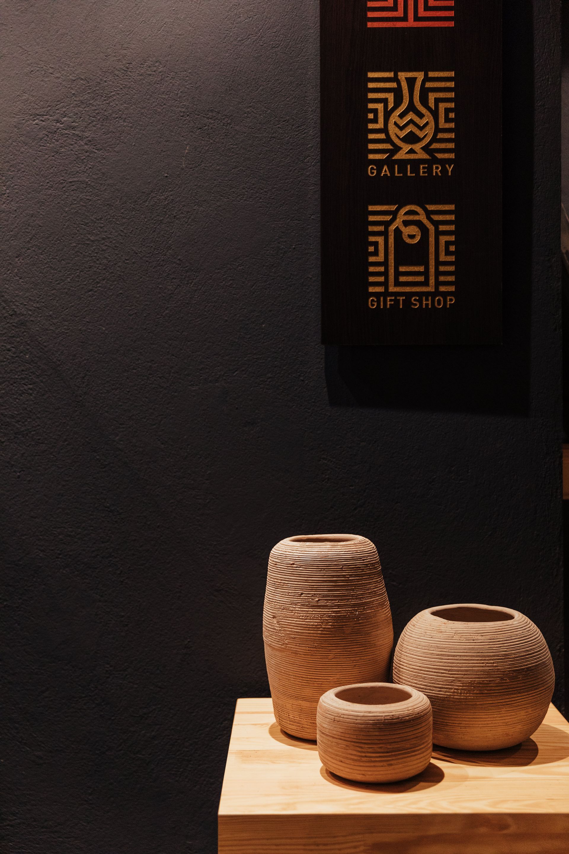 Tres jarrones están sobre una mesa de madera frente a una pared negra.