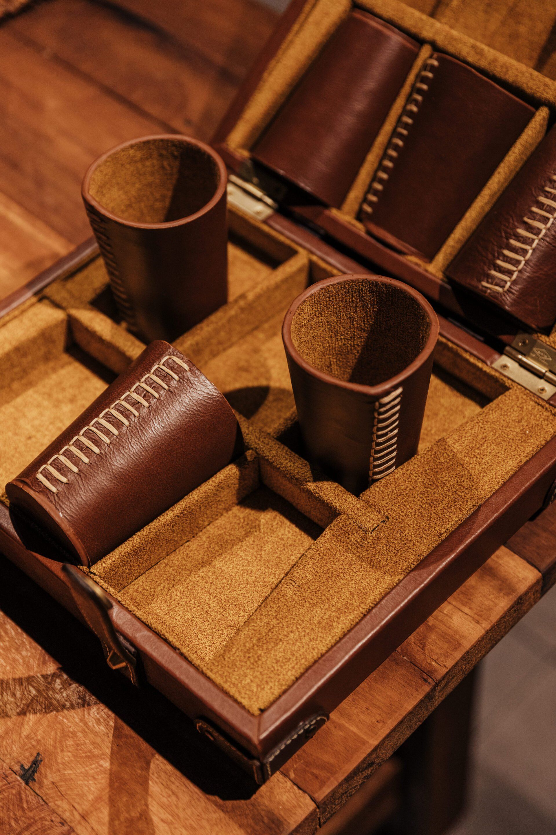 Dos tazas de cuero marrón están colocadas encima de una bandeja de madera.