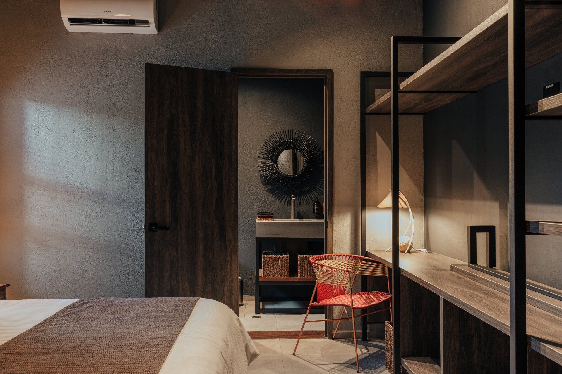 Un dormitorio con una cama, silla, escritorio y estantes.