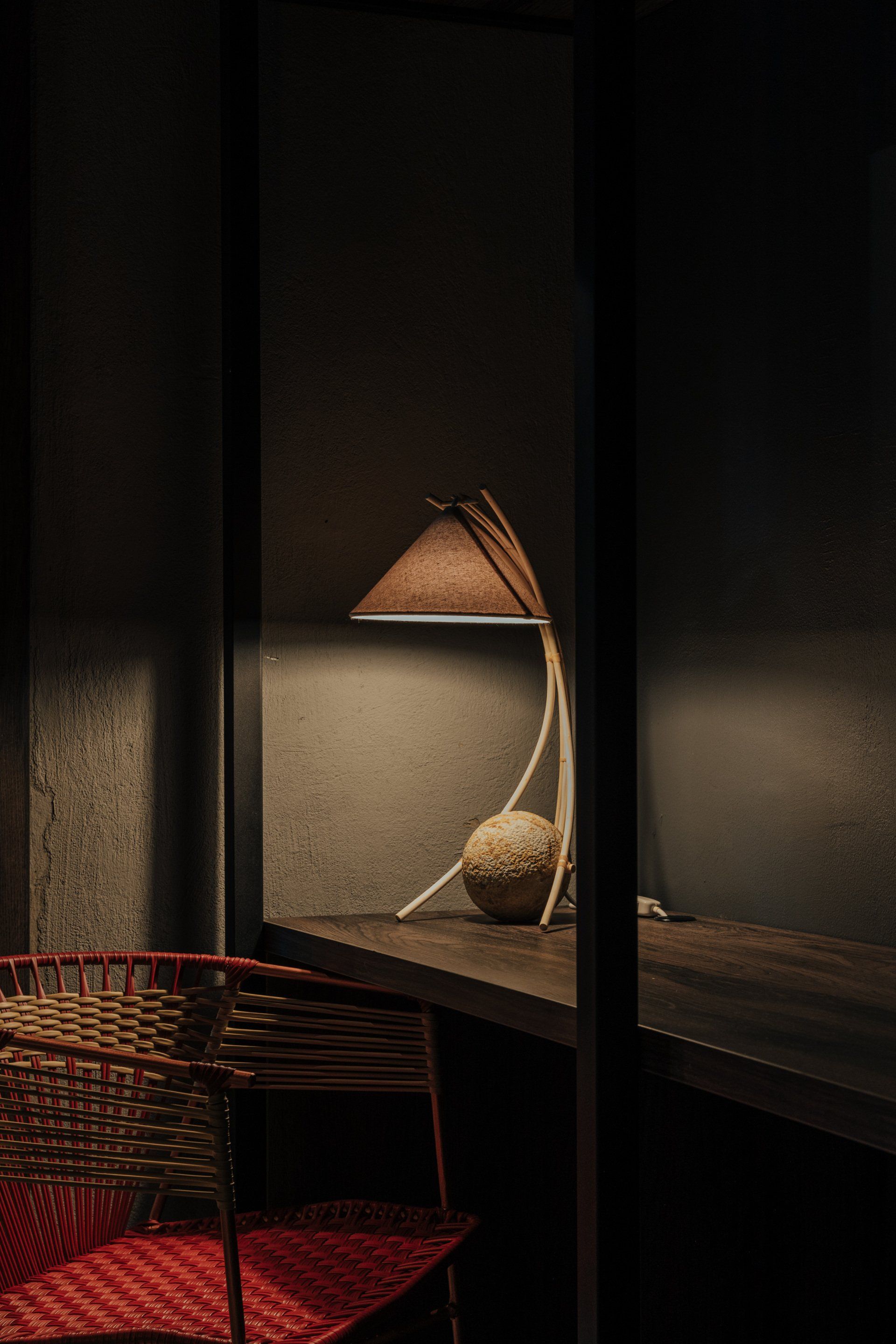 Una lámpara está sobre una mesa al lado de una silla en una habitación oscura.