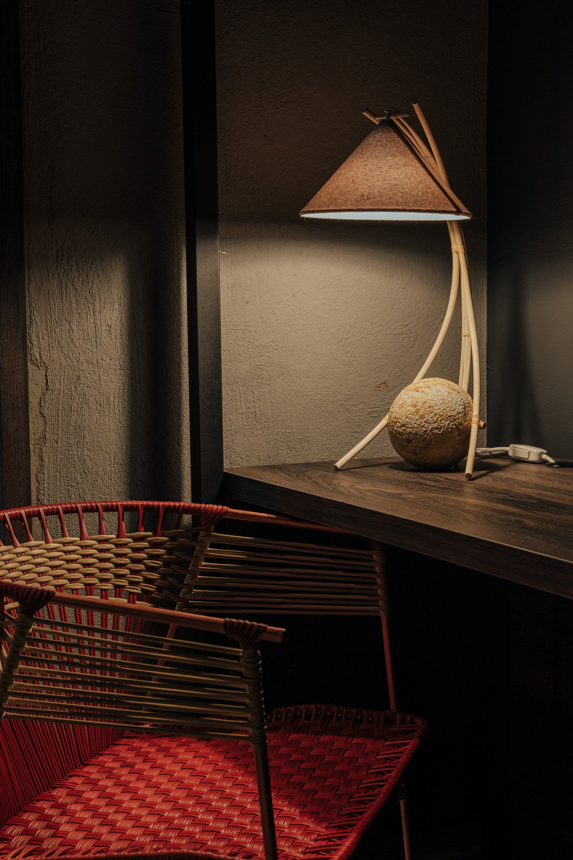 Una lámpara está sobre una mesa de madera al lado de una silla de mimbre.