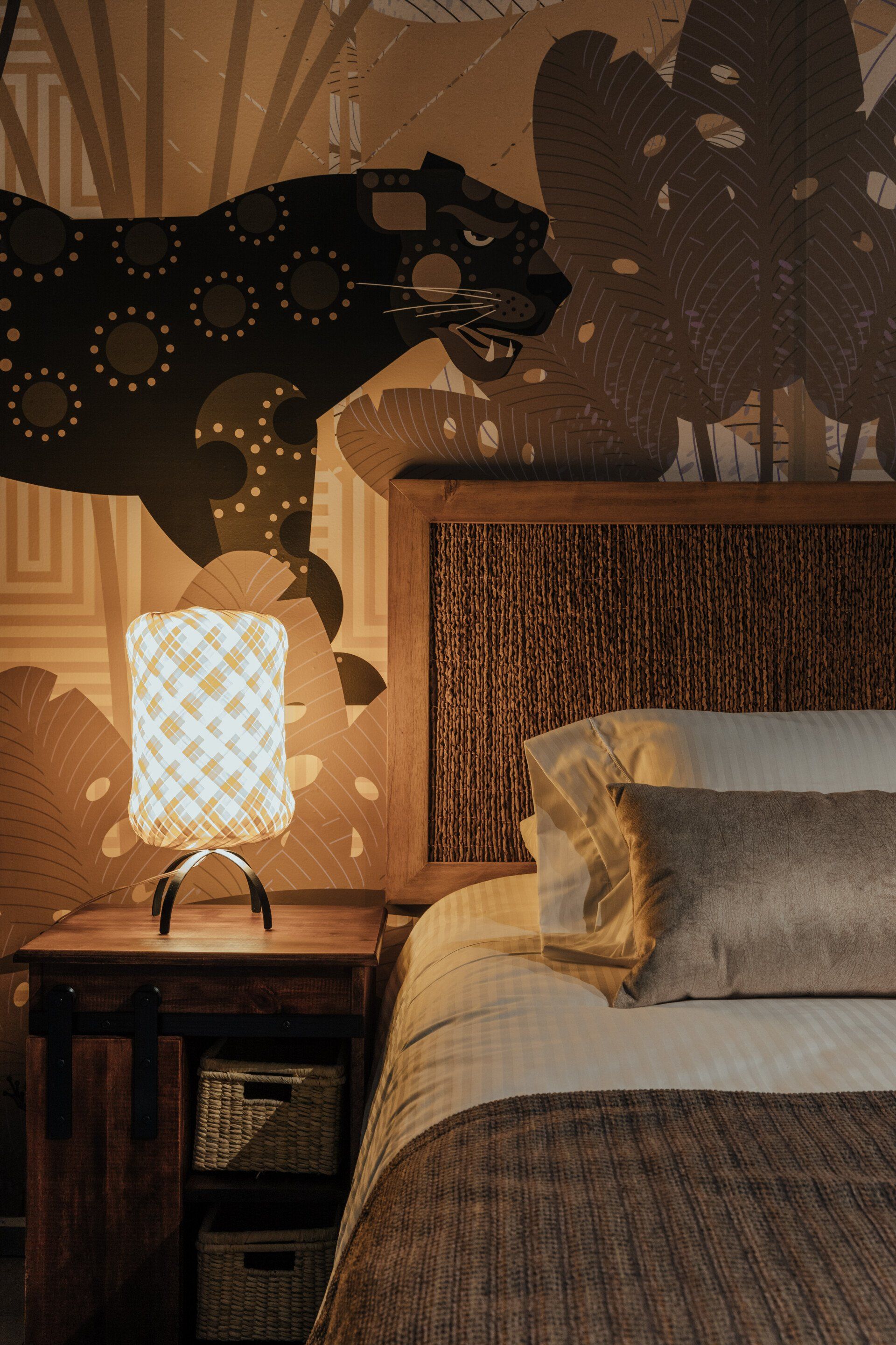 Un dormitorio con una cama, mesita de noche, lámpara y una pantera en la pared.