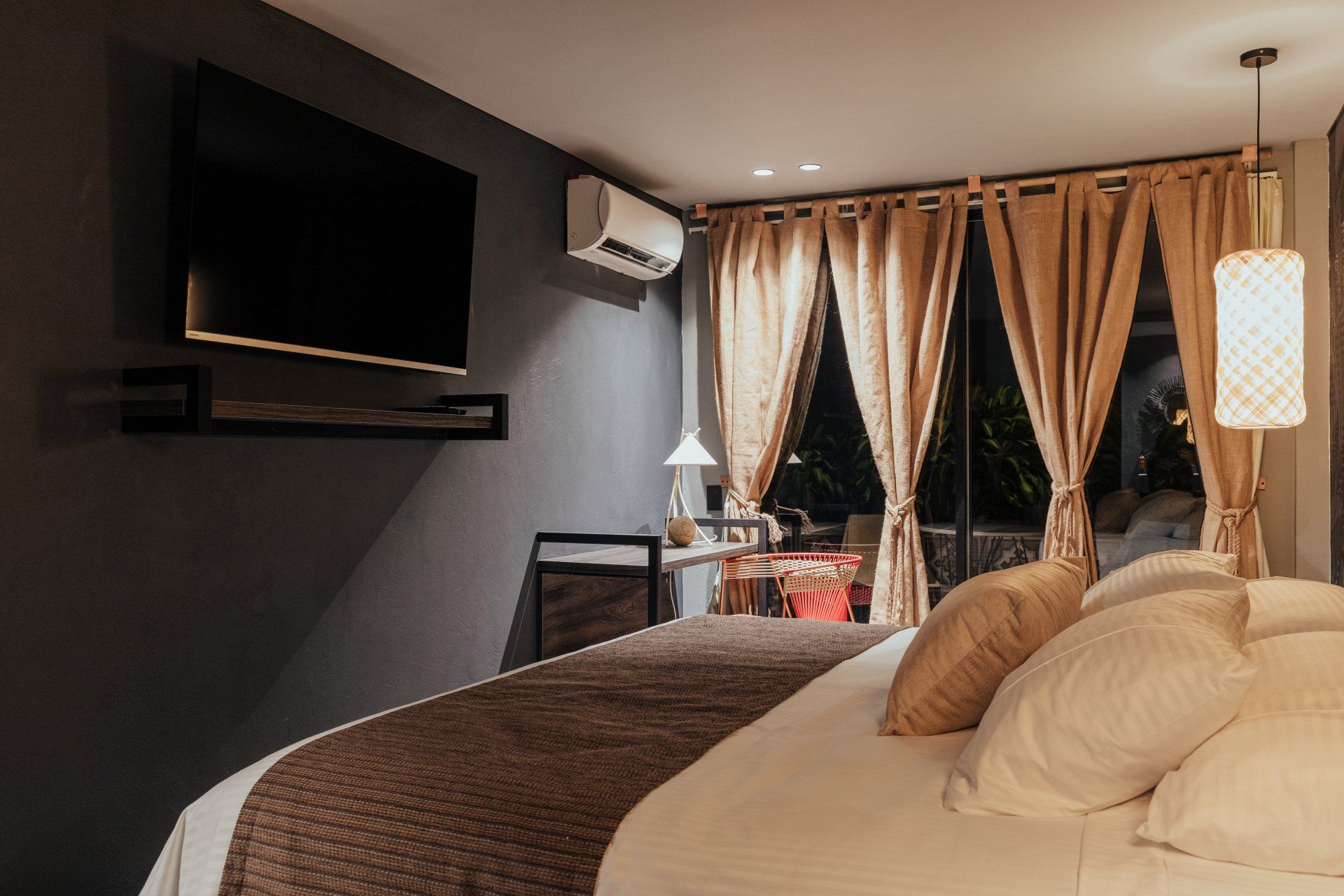 Un dormitorio con una cama, televisión, cortinas y una ventana.