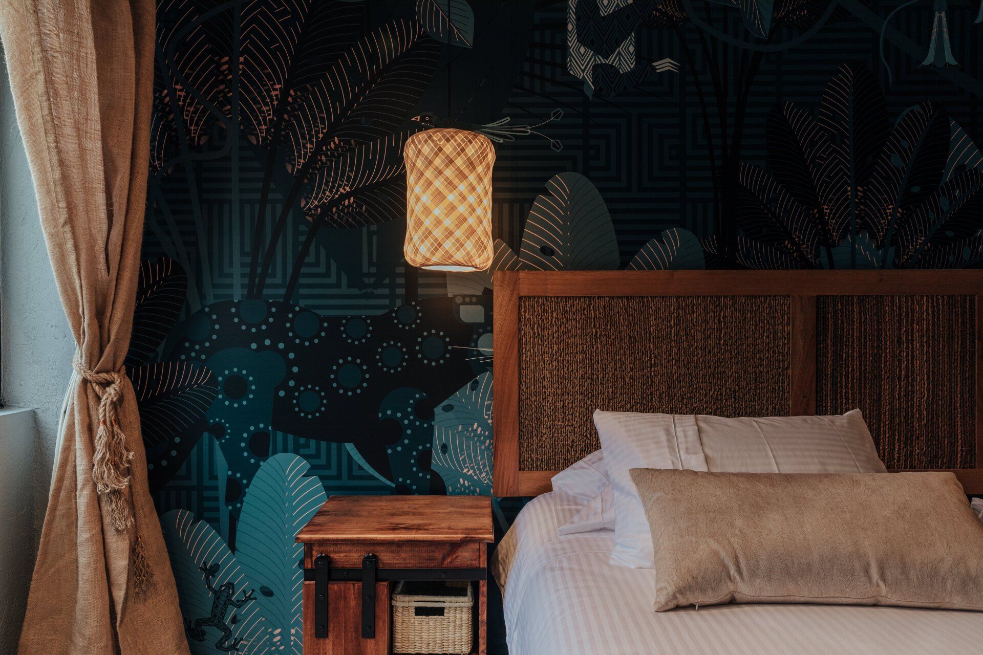 Un dormitorio con cama, mesita de noche, lámpara y papel pintado en la pared.