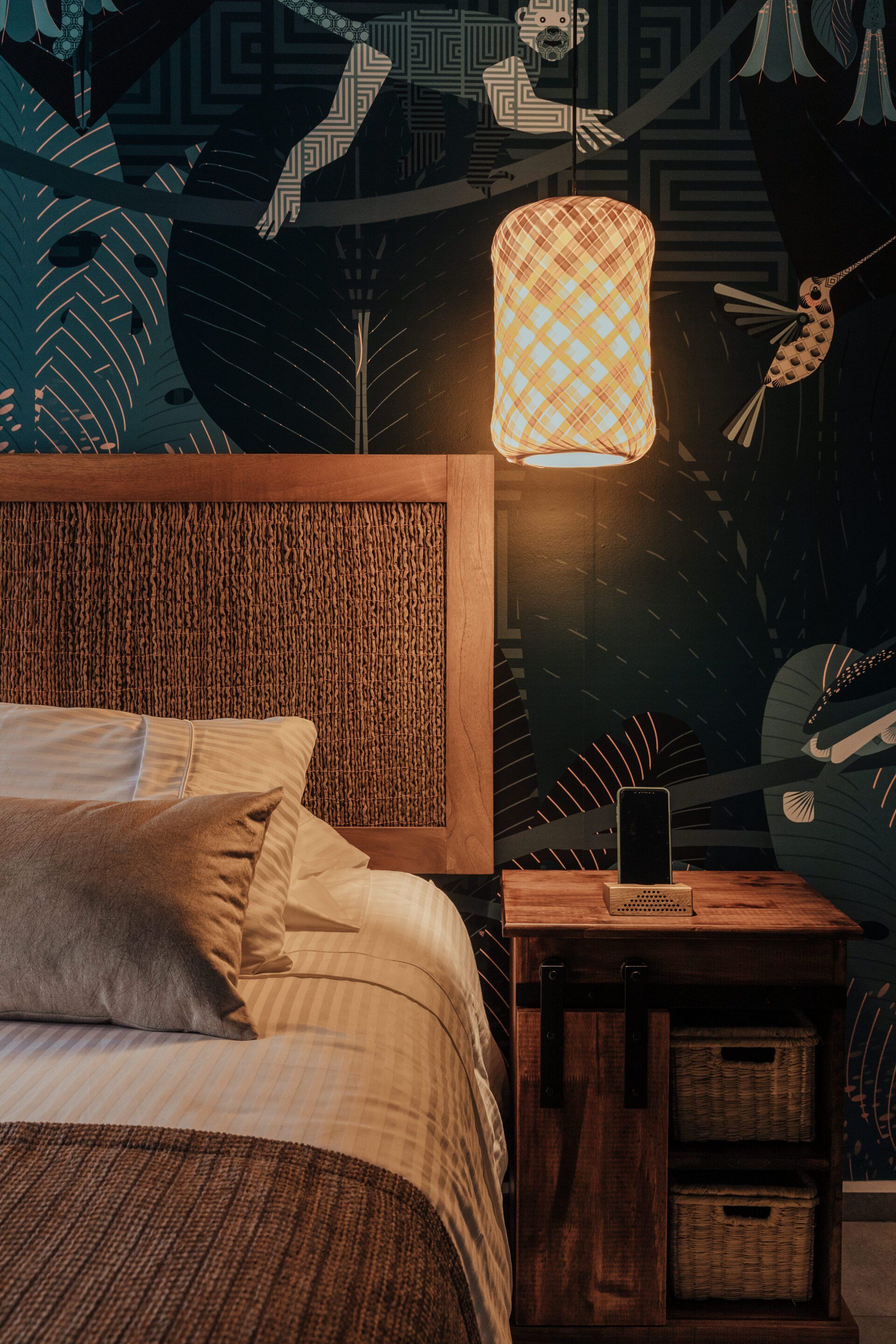 Un dormitorio con cama, mesita de noche, lámpara y cuadro en la pared.