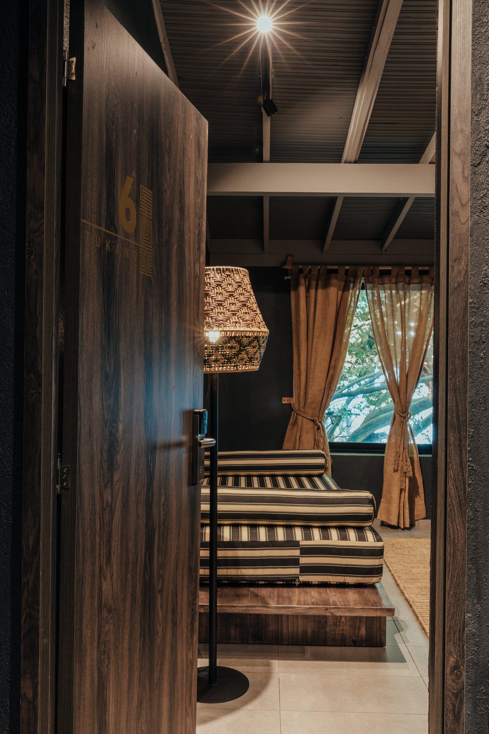 Una puerta de madera se abre a un dormitorio con una lámpara y una cama.