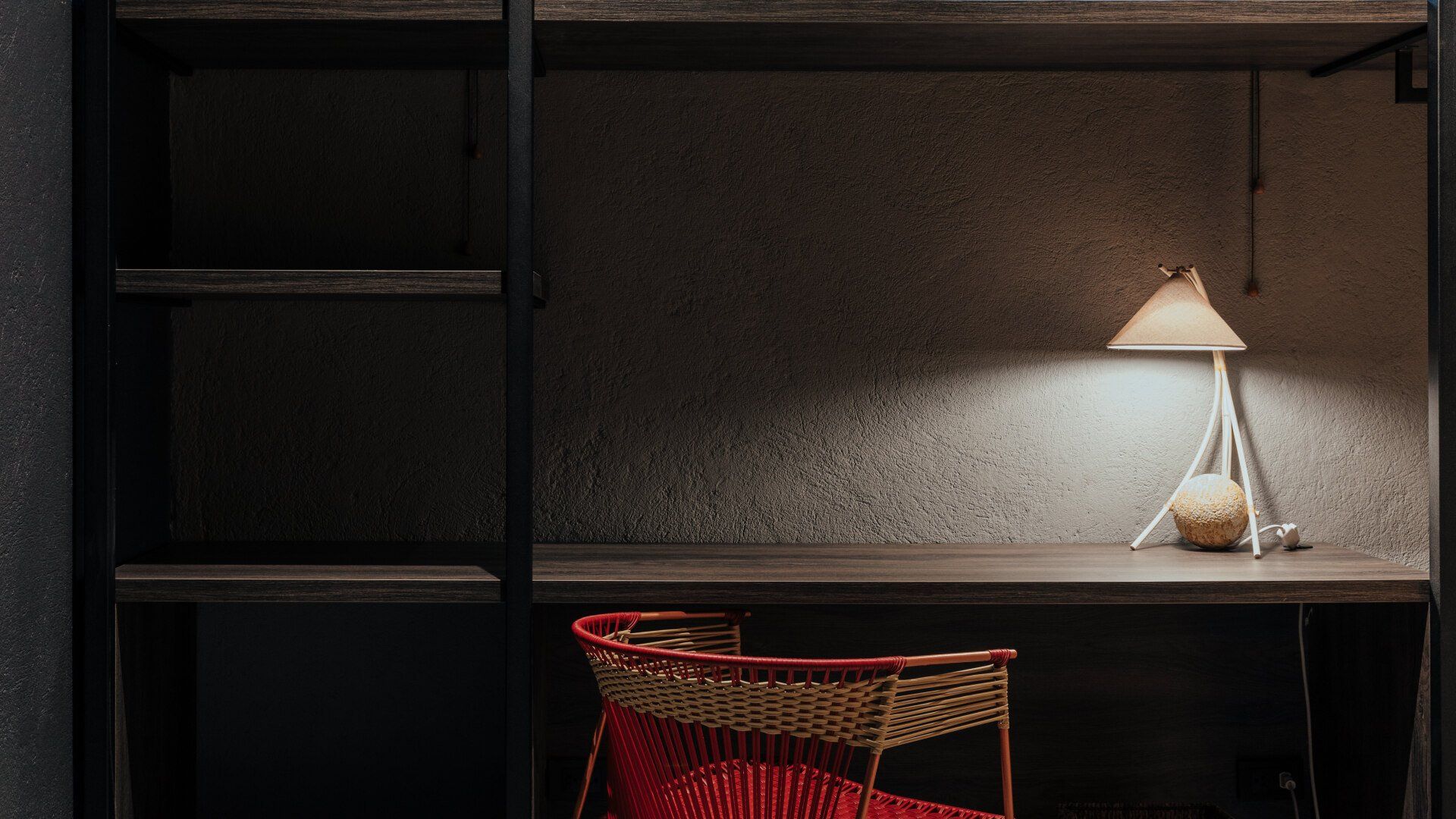 Un escritorio con una silla y una lámpara encima en una habitación oscura.