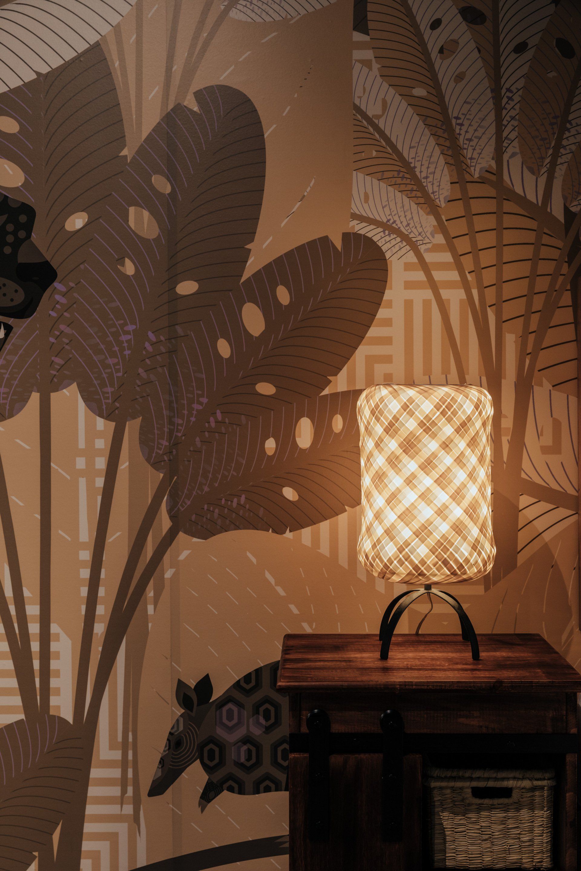 Una lámpara está colocada sobre una mesa frente a una pared con hojas sobre ella.