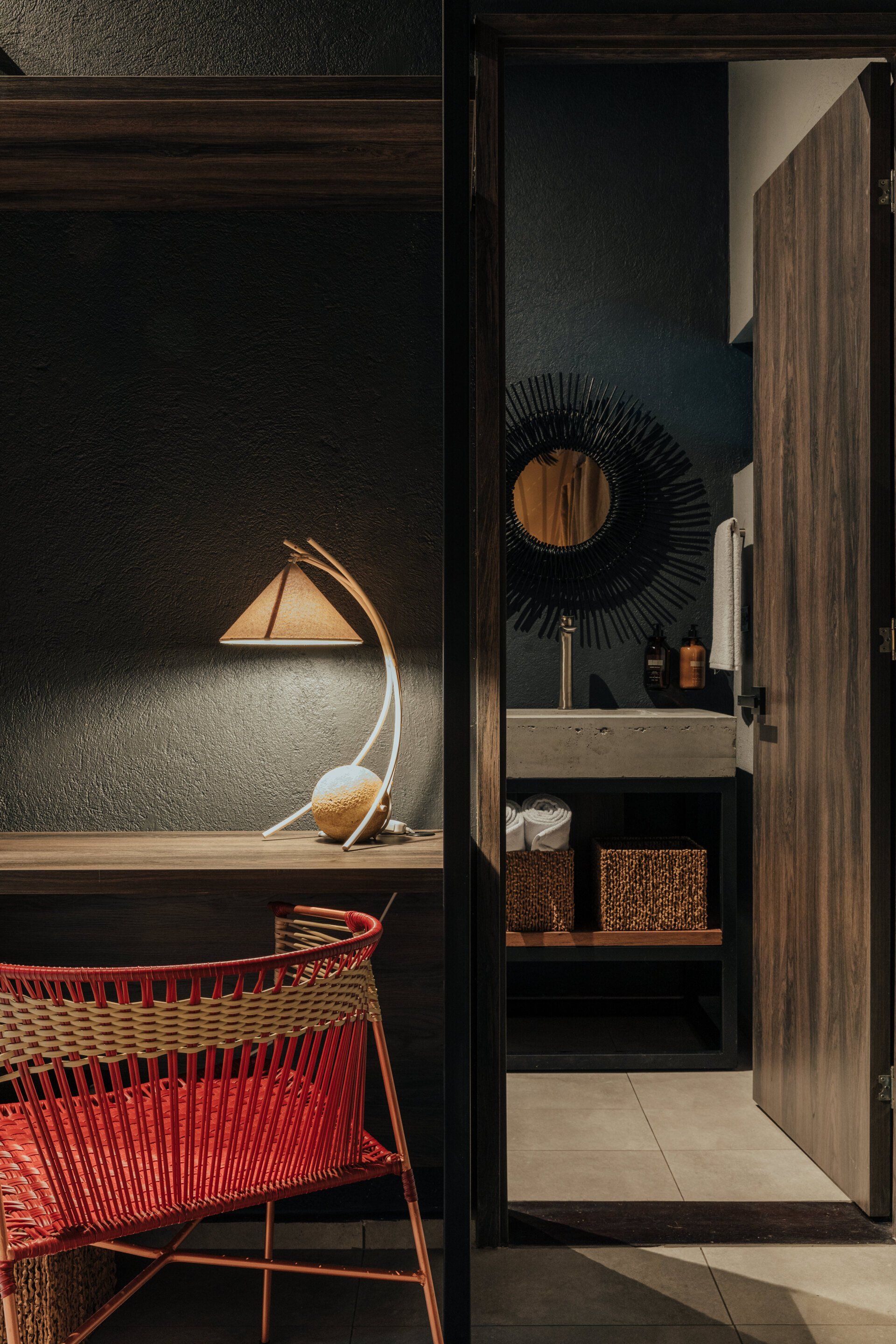 Una silla de mimbre está junto a un escritorio en una habitación contigua a un baño.