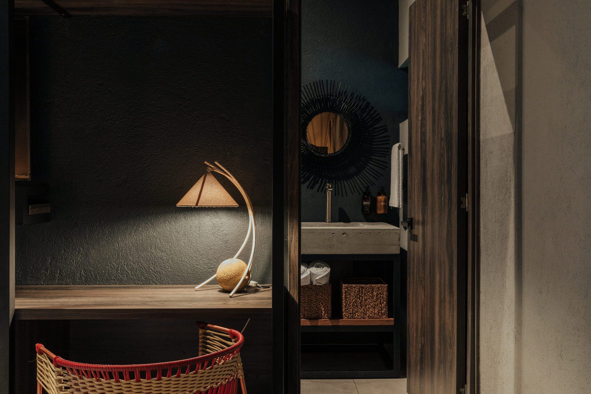 Una habitación con escritorio, silla, lámpara y baño.