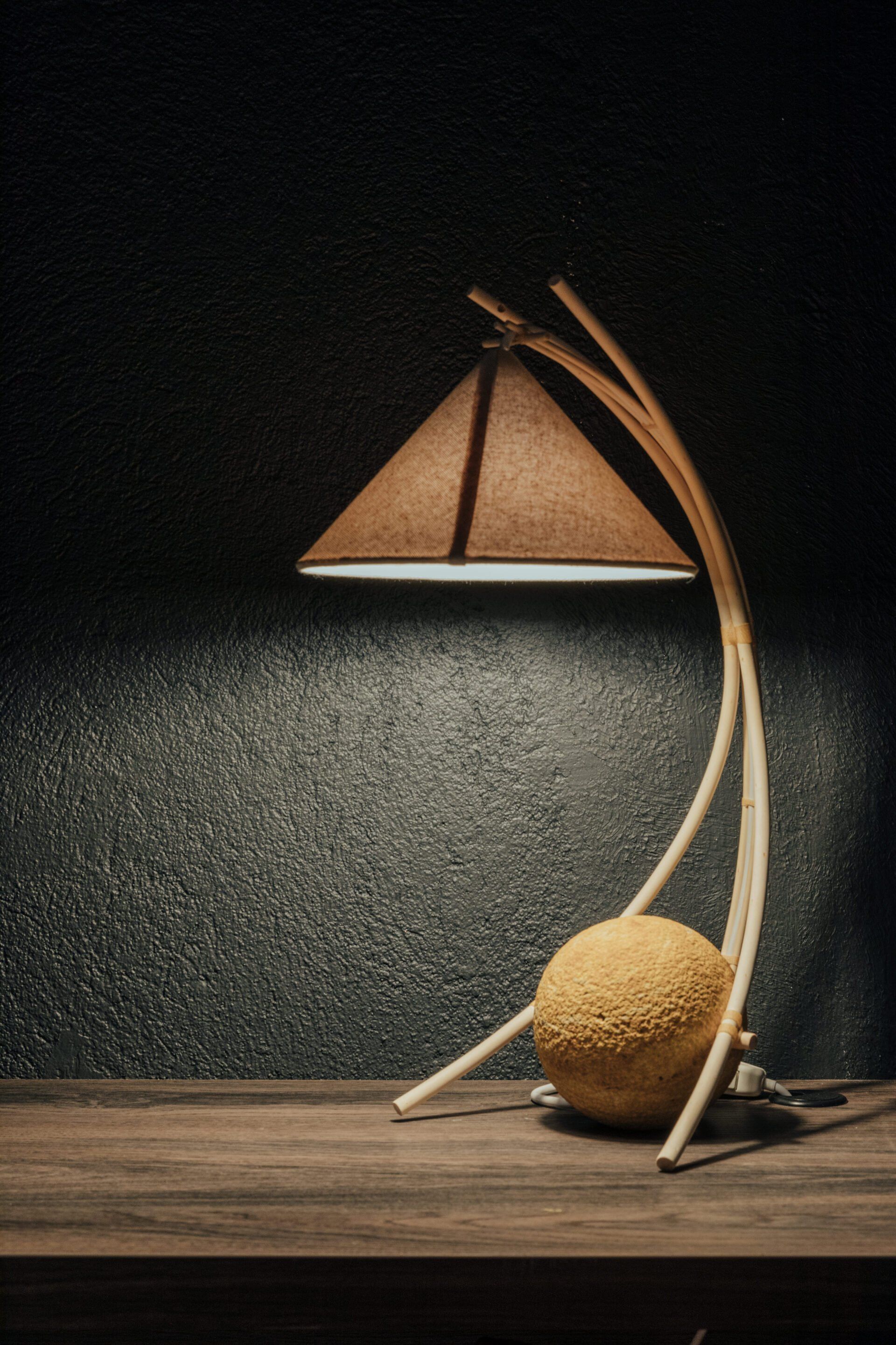 Una lámpara con pantalla en forma de triángulo está sobre una mesa de madera.