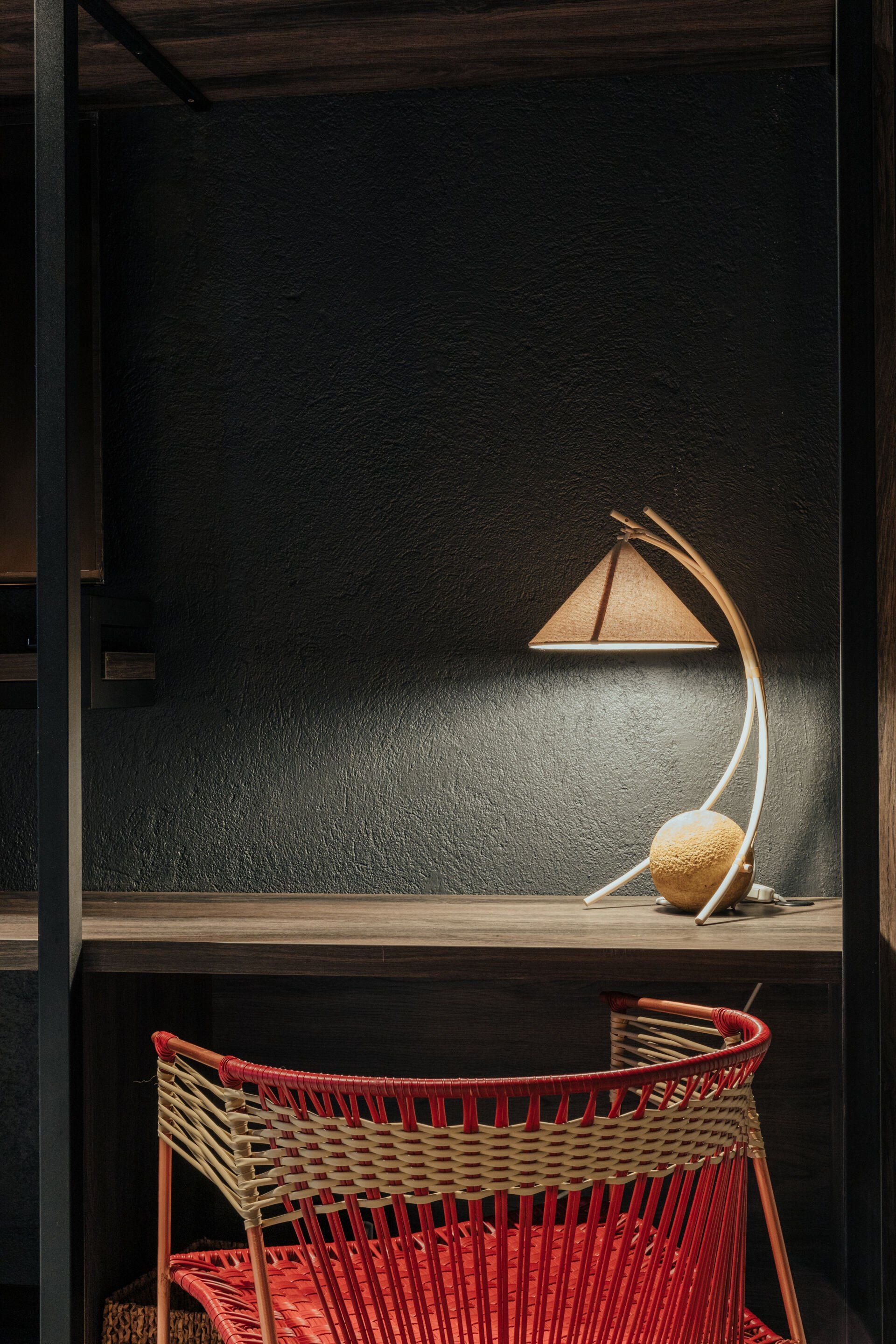 Una silla roja está frente a un escritorio con una lámpara encima.