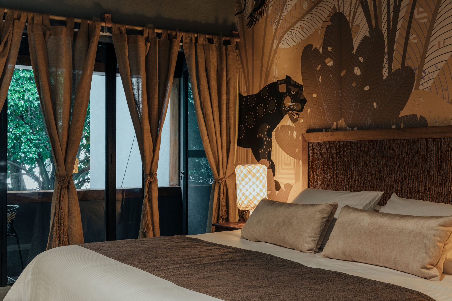 Un dormitorio con una cama, cortinas, una lámpara y una pantera en la pared.