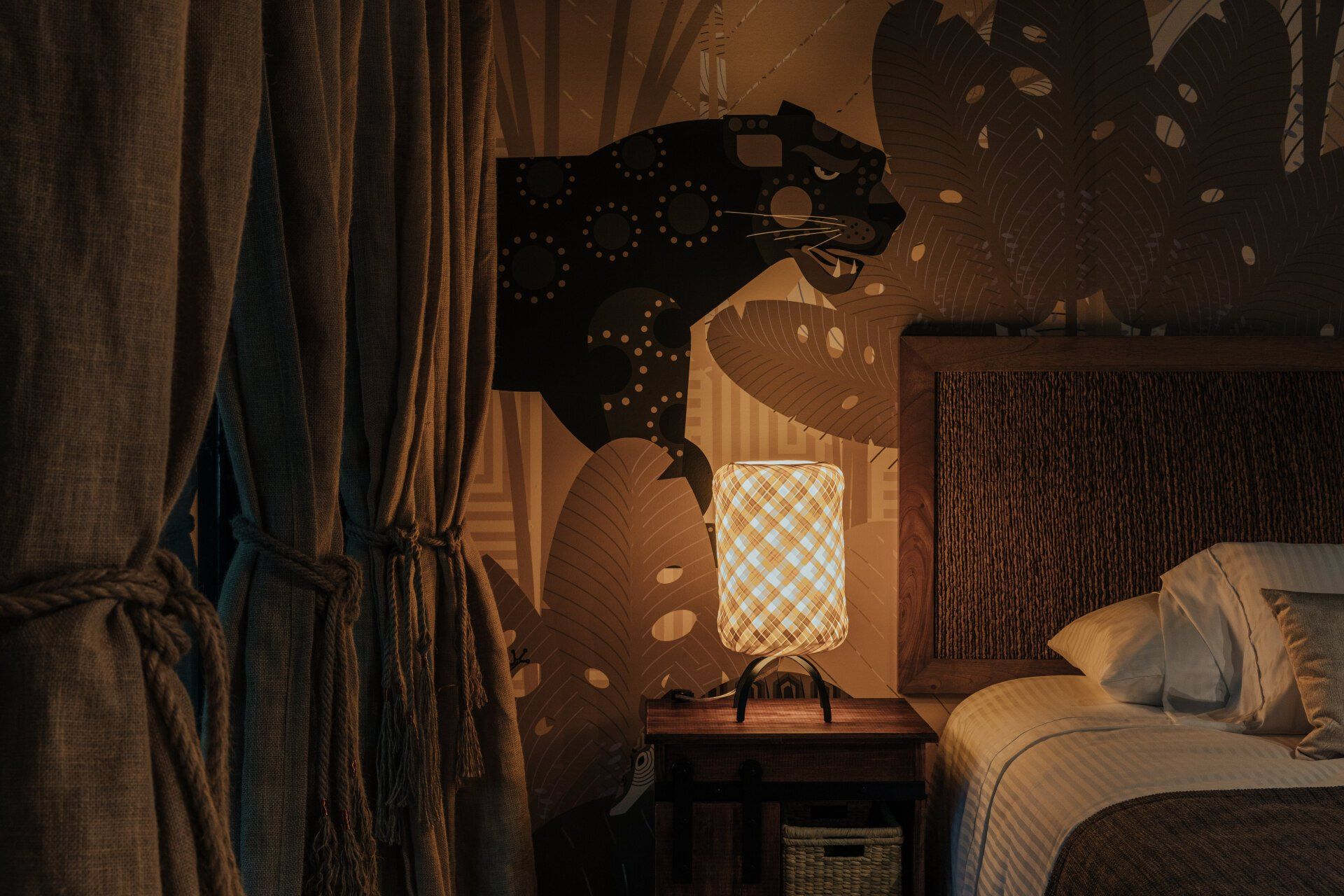 Un dormitorio con una cama, mesita de noche, lámpara y una cabeza de pantera en la pared.