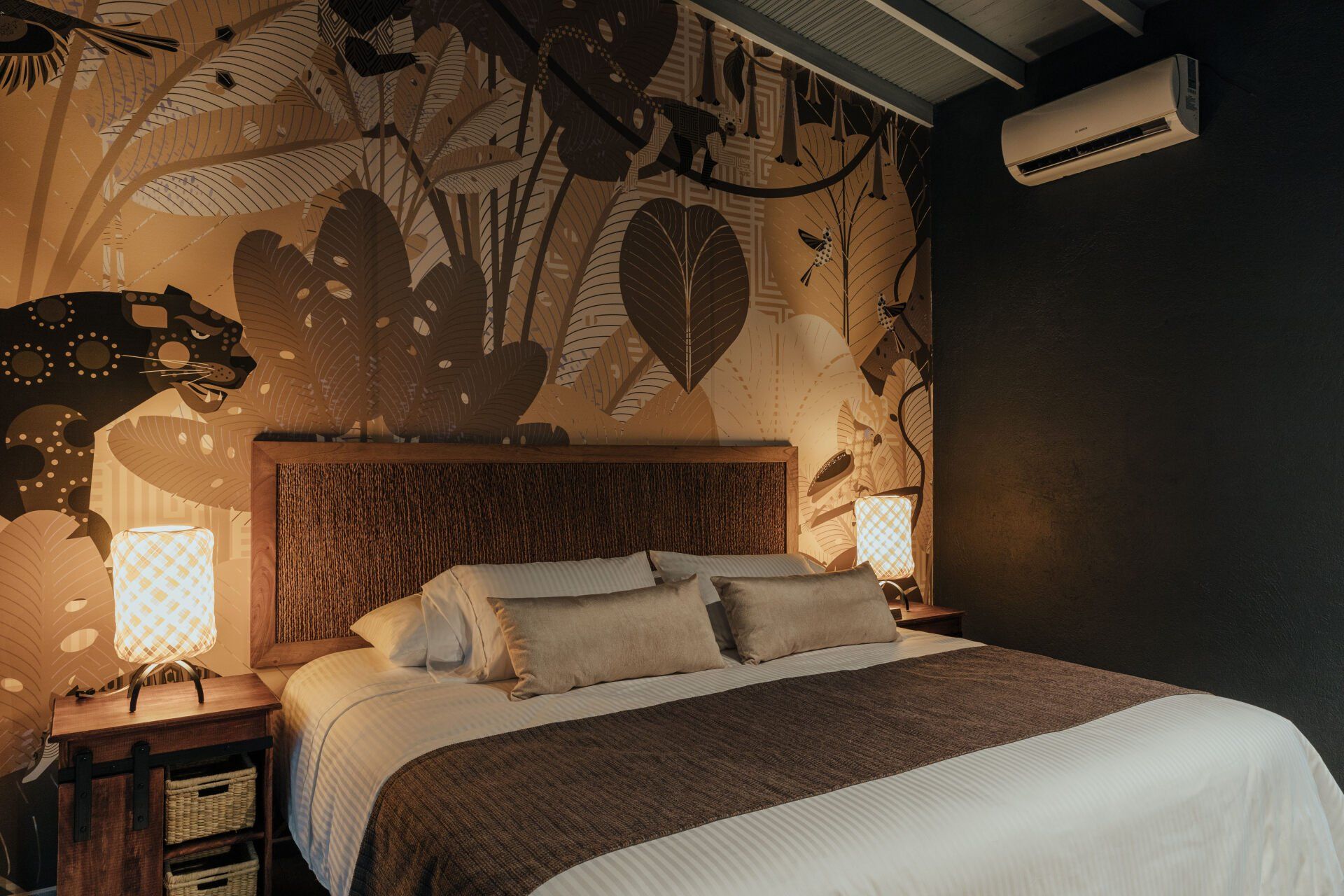 Un dormitorio con una cama, mesitas de noche, lámparas y un mural en la pared.