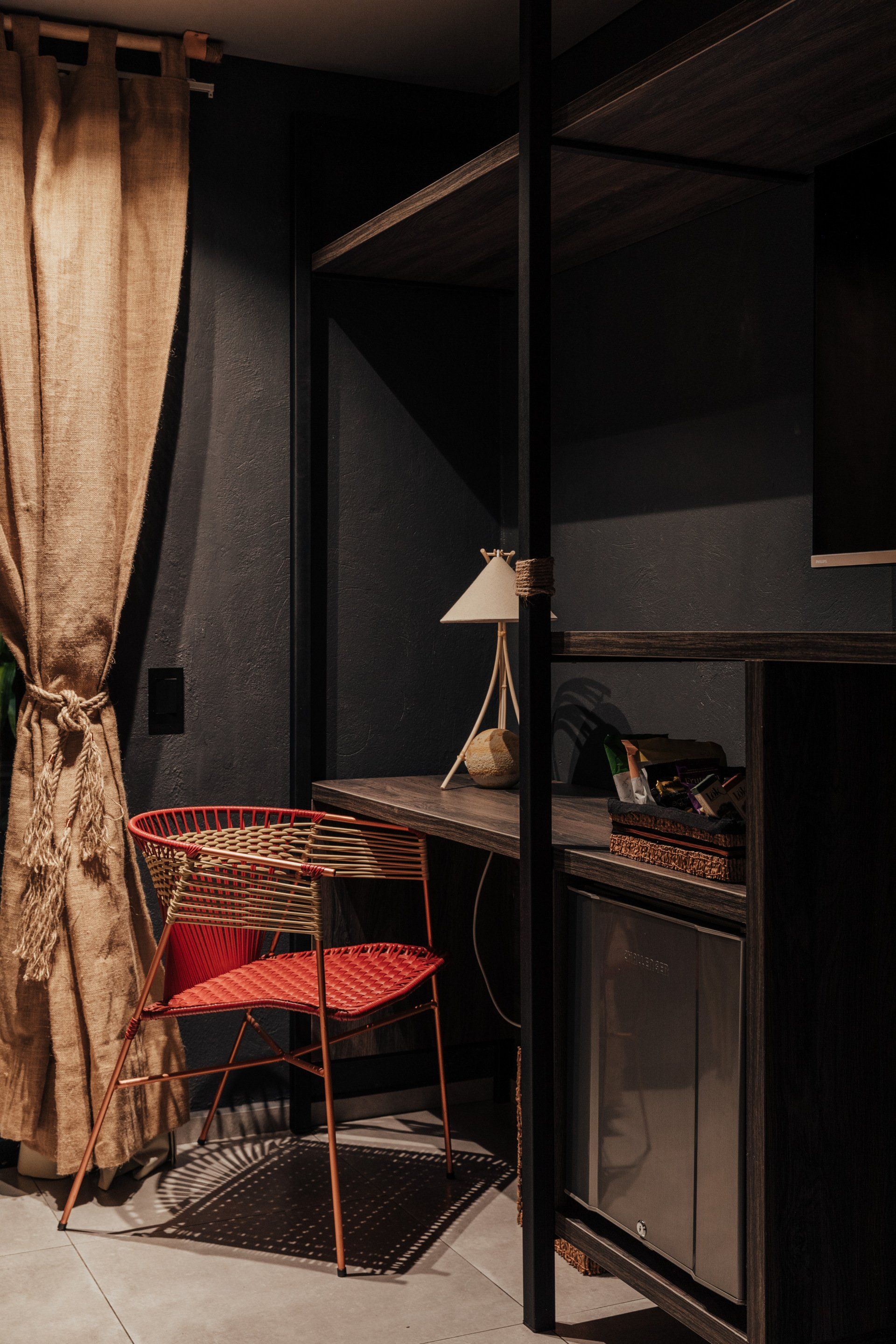 Una habitación con un escritorio, una silla, una lámpara y un refrigerador.