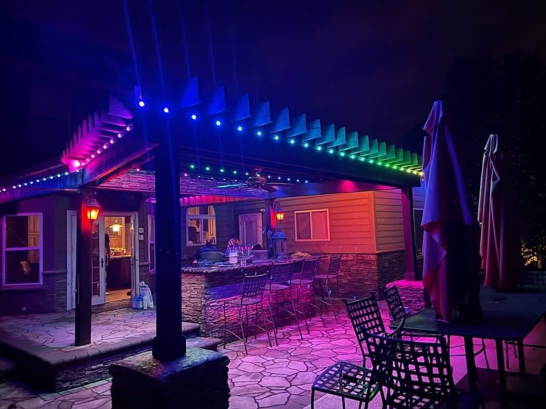 A patio with a pergola and lights at night.
