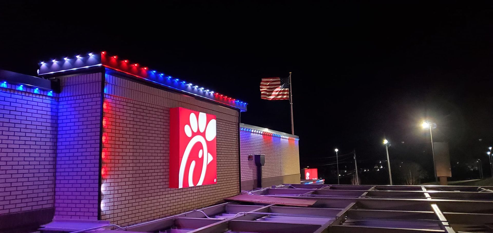 A chick-fil-a restaurant is lit up with red , white and blue lights at night.