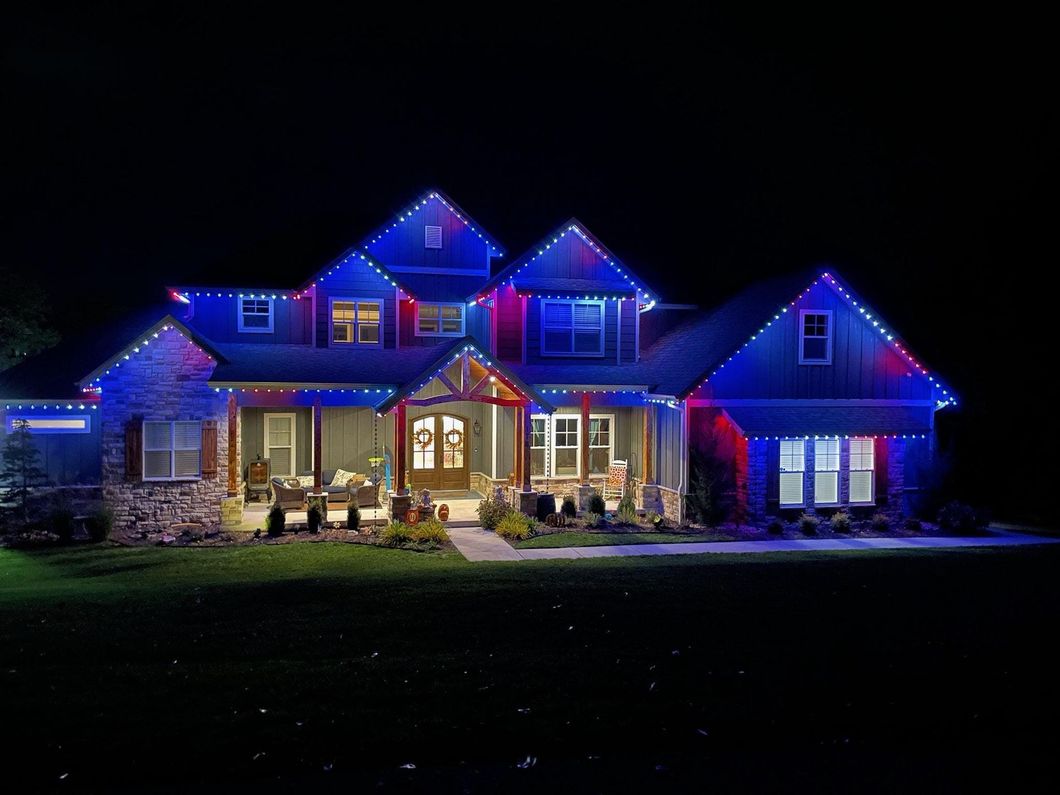 A large house is lit up with red , white and blue christmas lights.
