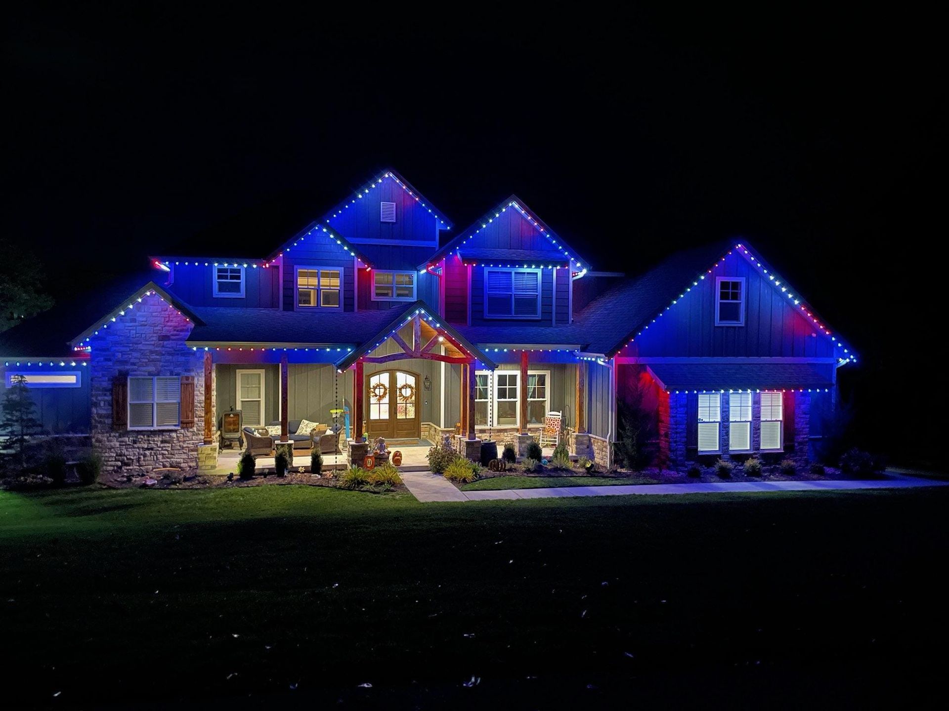 A large house is lit up with red , white and blue christmas lights.