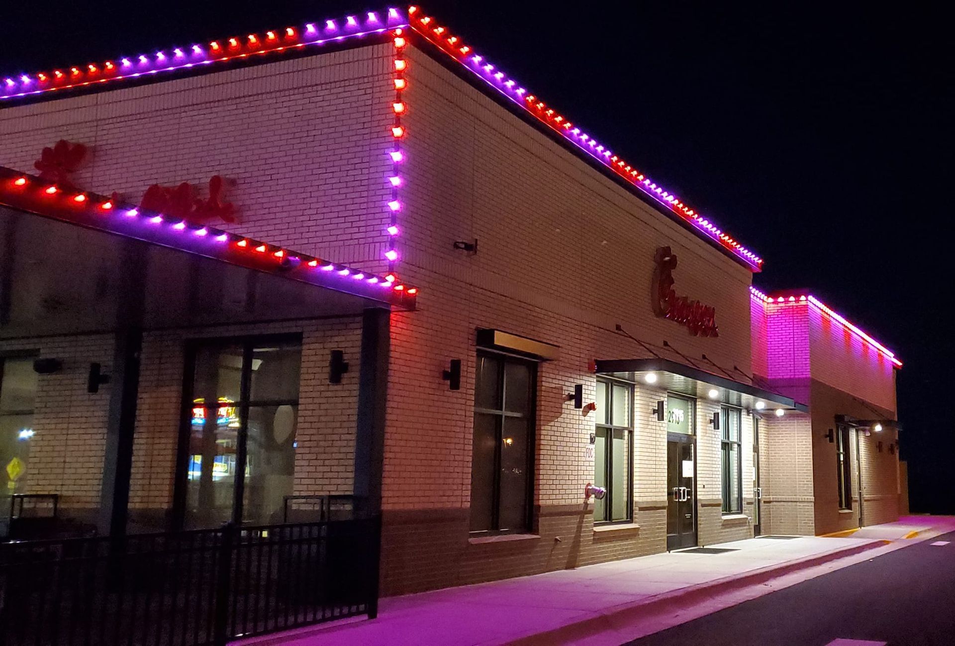 A chick-fil-a restaurant is lit up at night with purple and red lights.