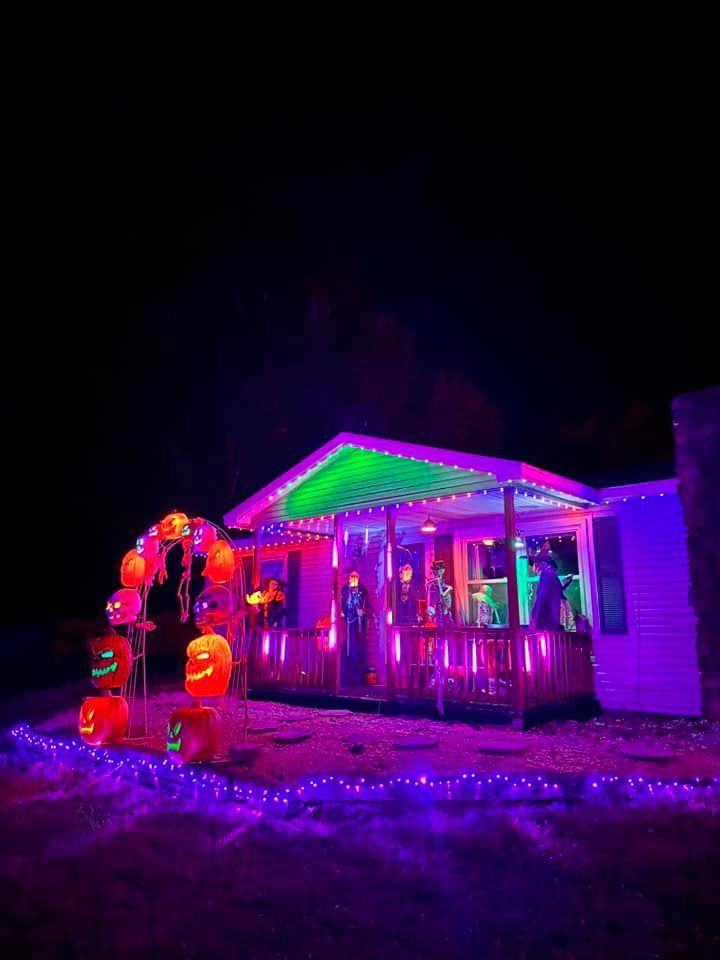 A house decorated for halloween with purple and green lights and pumpkins.
