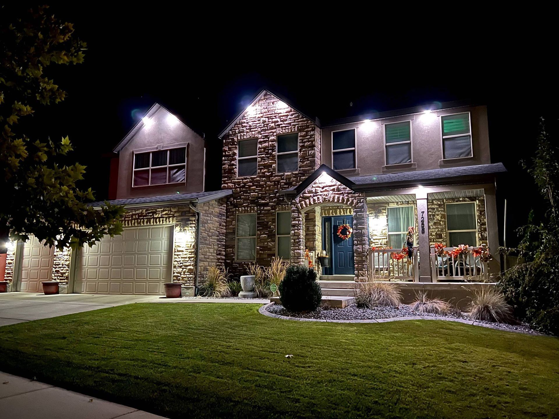 A large house is lit up at night and has a lush green lawn in front of it.